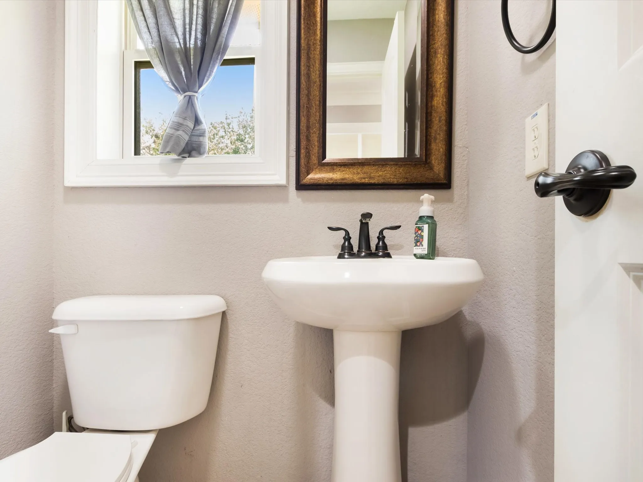 Pedestal sink with oil-rubbed bronze faucet, framed mirror, and white window trim