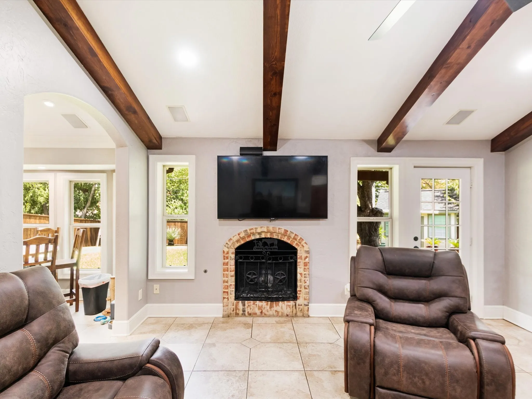 Exposed wood ceiling beams, a brick-surround fireplace with an iron grate, and light tile flooring