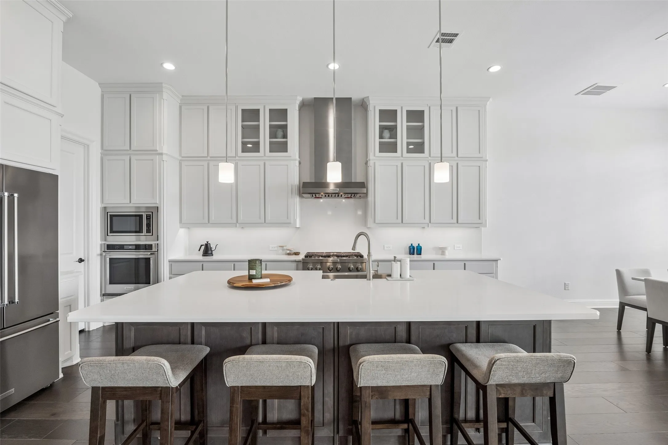 Expansive kitchen island with seating, stainless steel appliances, pendant lighting, shaker-style cabinetry, and wood-finish flooring