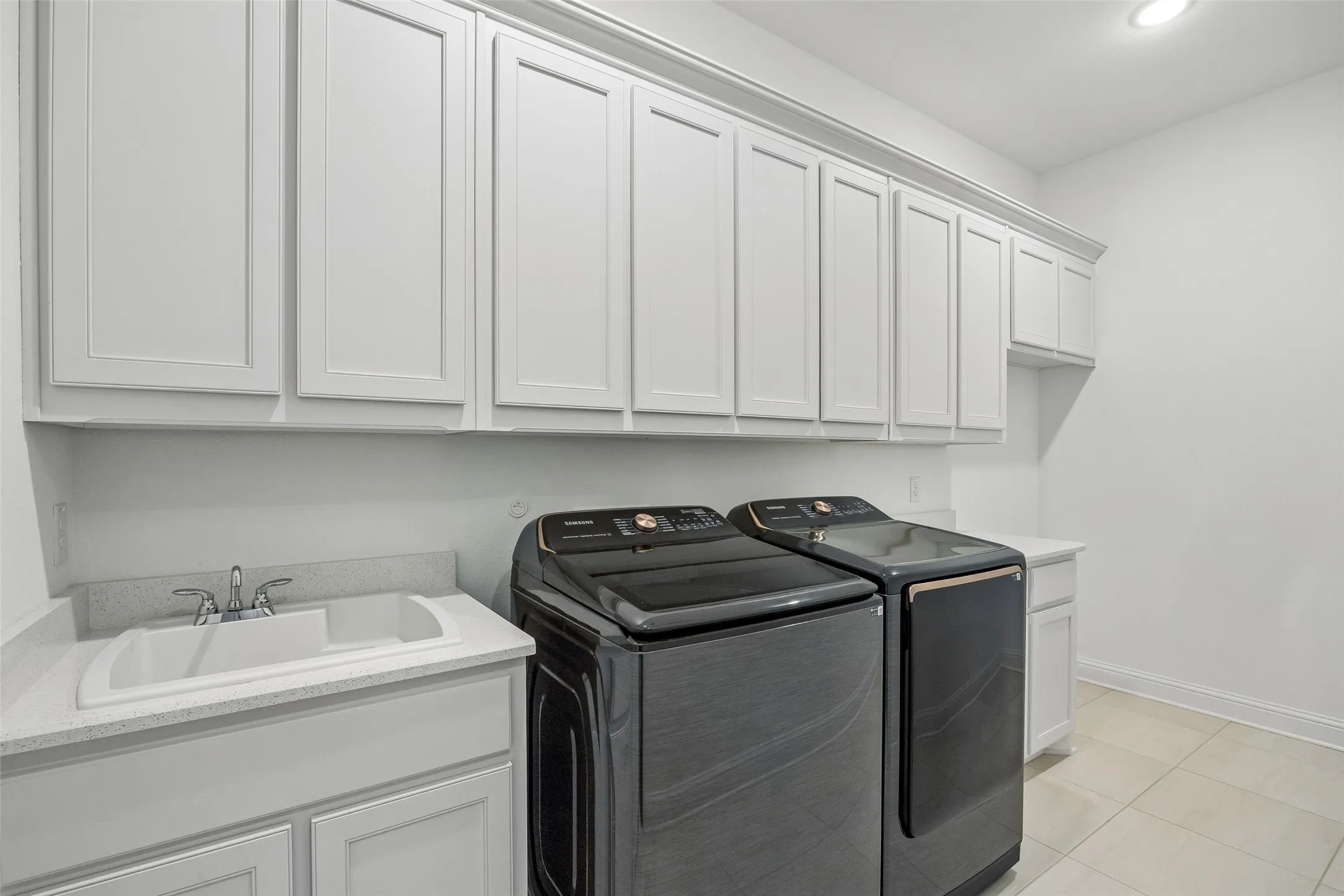 White cabinetry with crown molding, integrated utility sink, light-toned countertop, and tile flooring