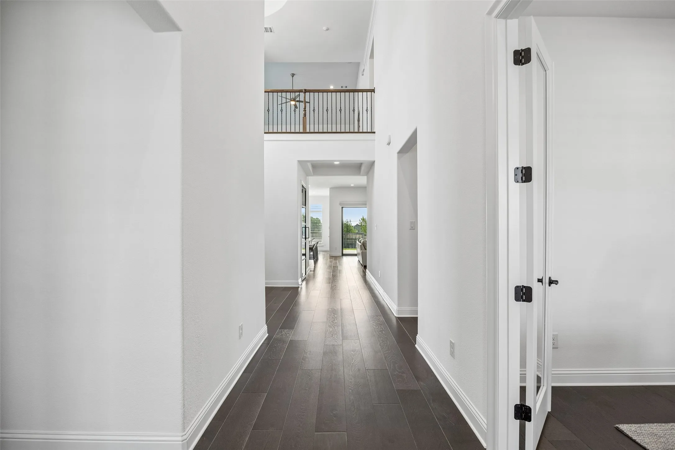 Hallway featuring wood-finish flooring, white trim, and a second-story balcony with wood and iron railing