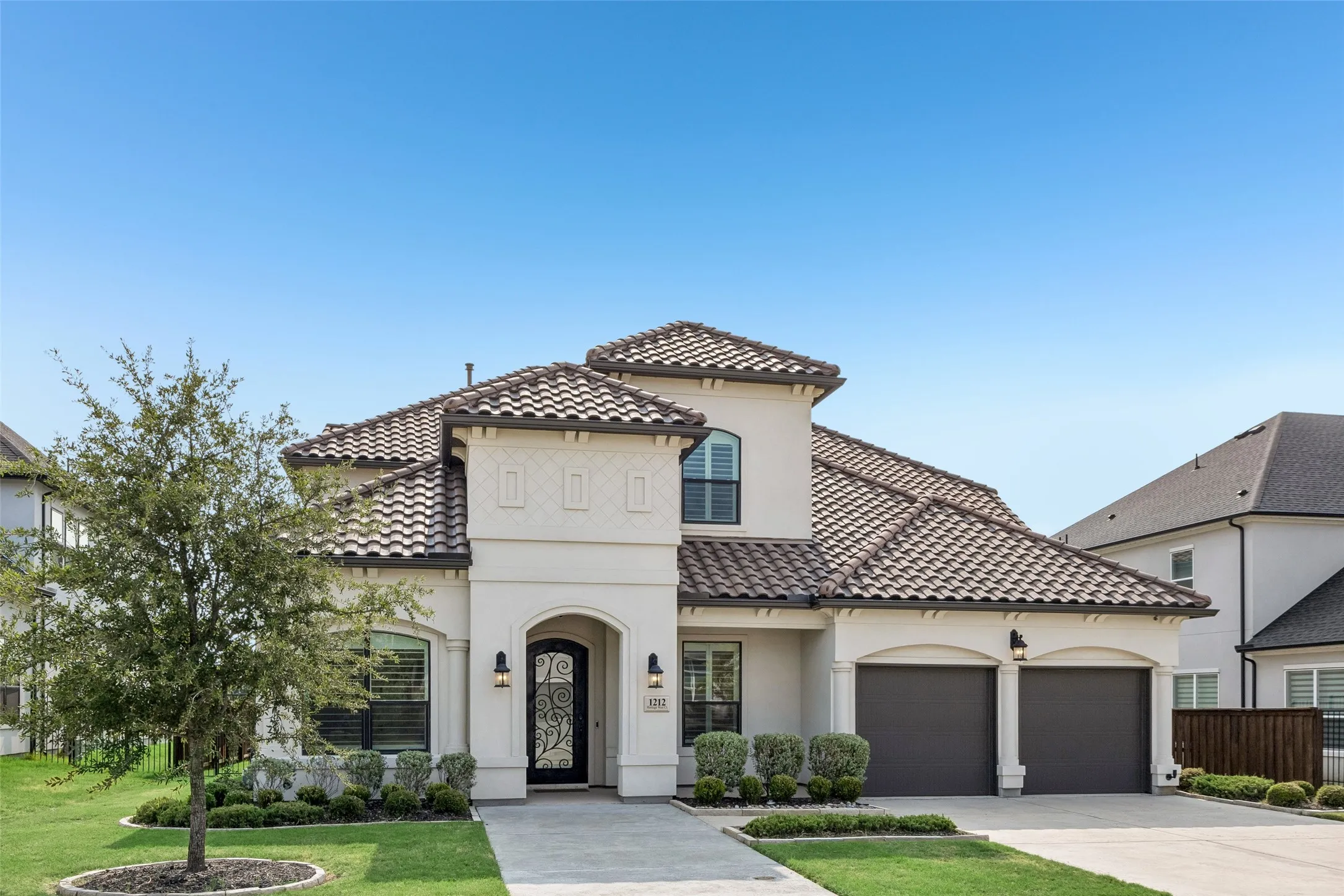 Stucco exterior with a tile roof, arched entry with an ornate iron door, and a two-car garage