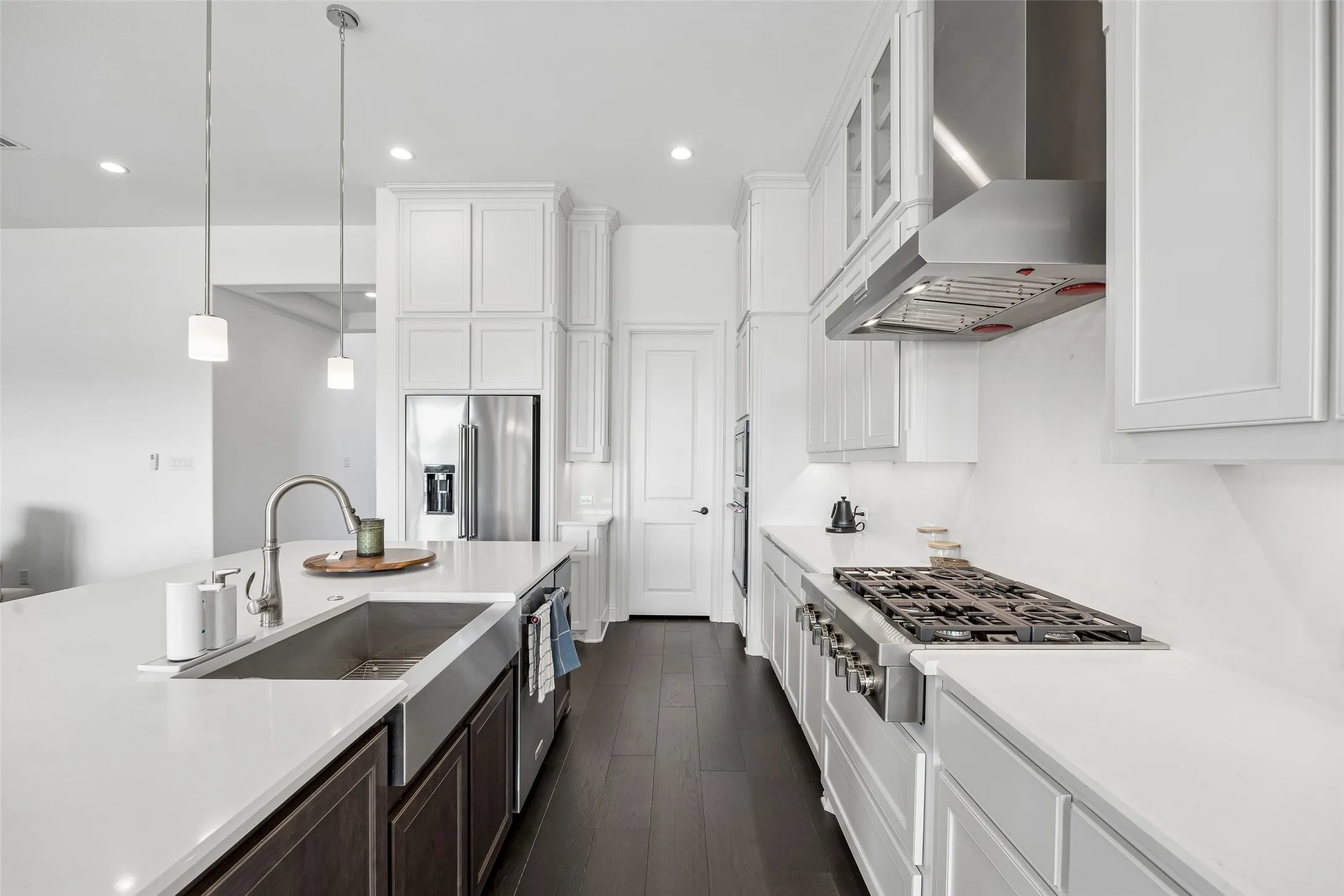 Gourmet kitchen featuring white shaker cabinetry, stainless steel appliances, dark wood-finish flooring, an expansive island with an undermount sink, and recessed lighting