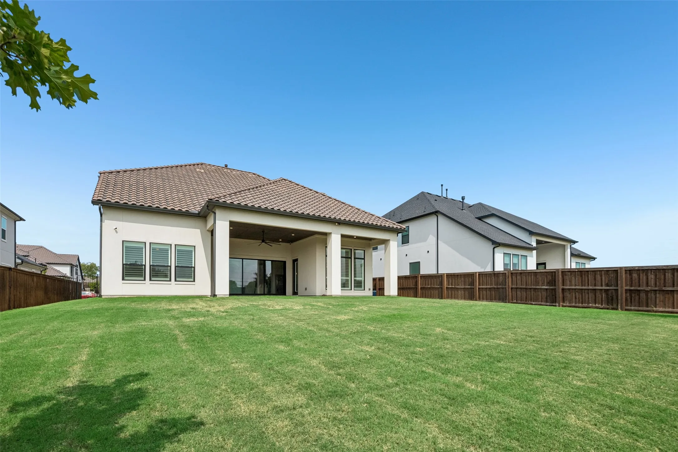 Expansive green lawn, covered patio with recessed lighting and a ceiling fan, sliding glass doors, multiple windows, and a wood privacy fence