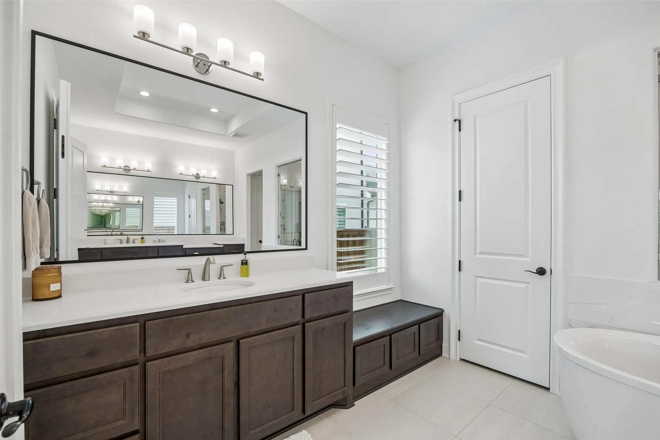 Expansive vanity with dark wood-finish cabinetry, a large frameless mirror, and a built-in window bench