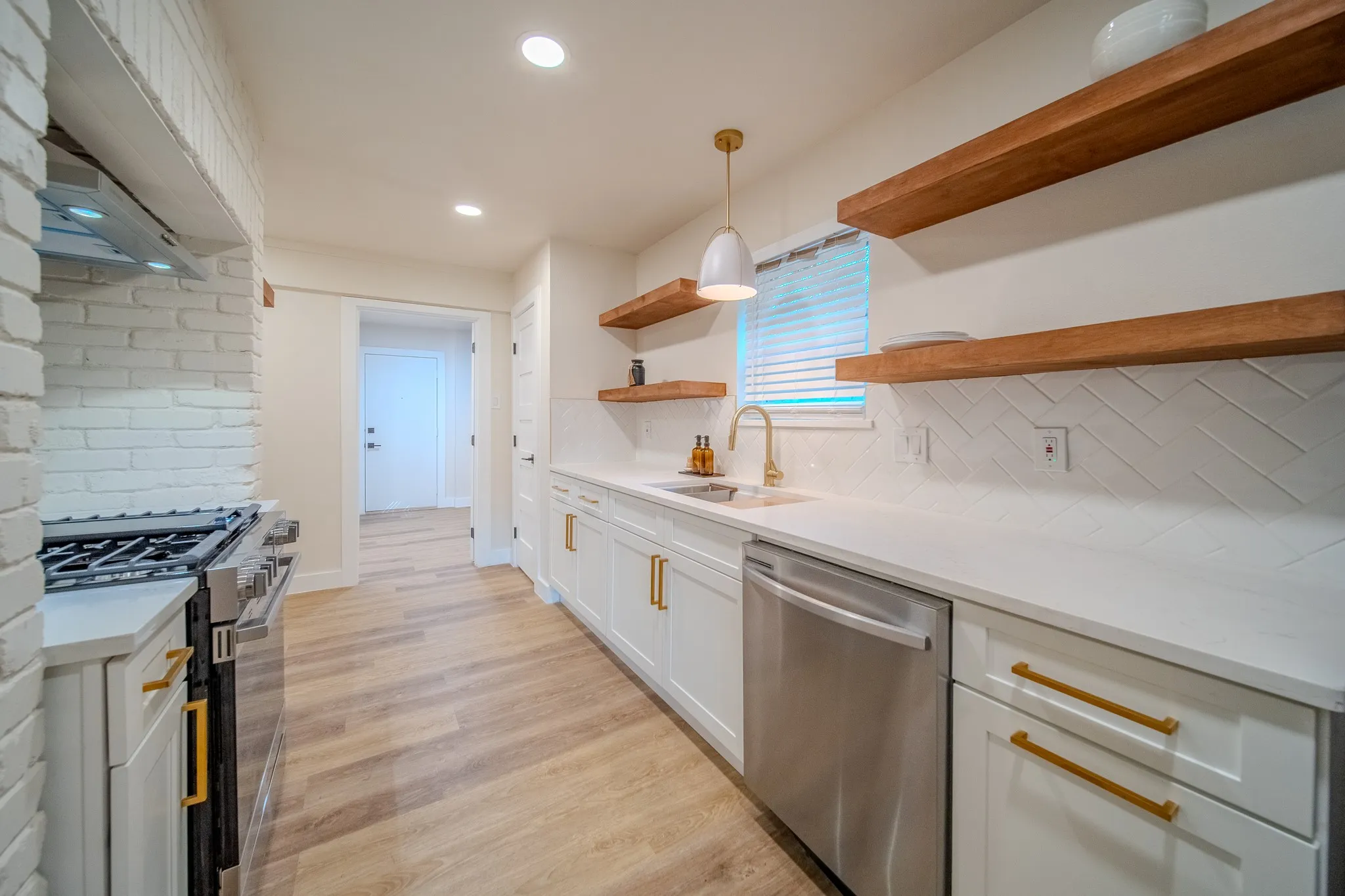 Modern kitchen featuring white shaker cabinetry, stainless steel appliances, a white herringbone tile backsplash, and wood-finish open shelving