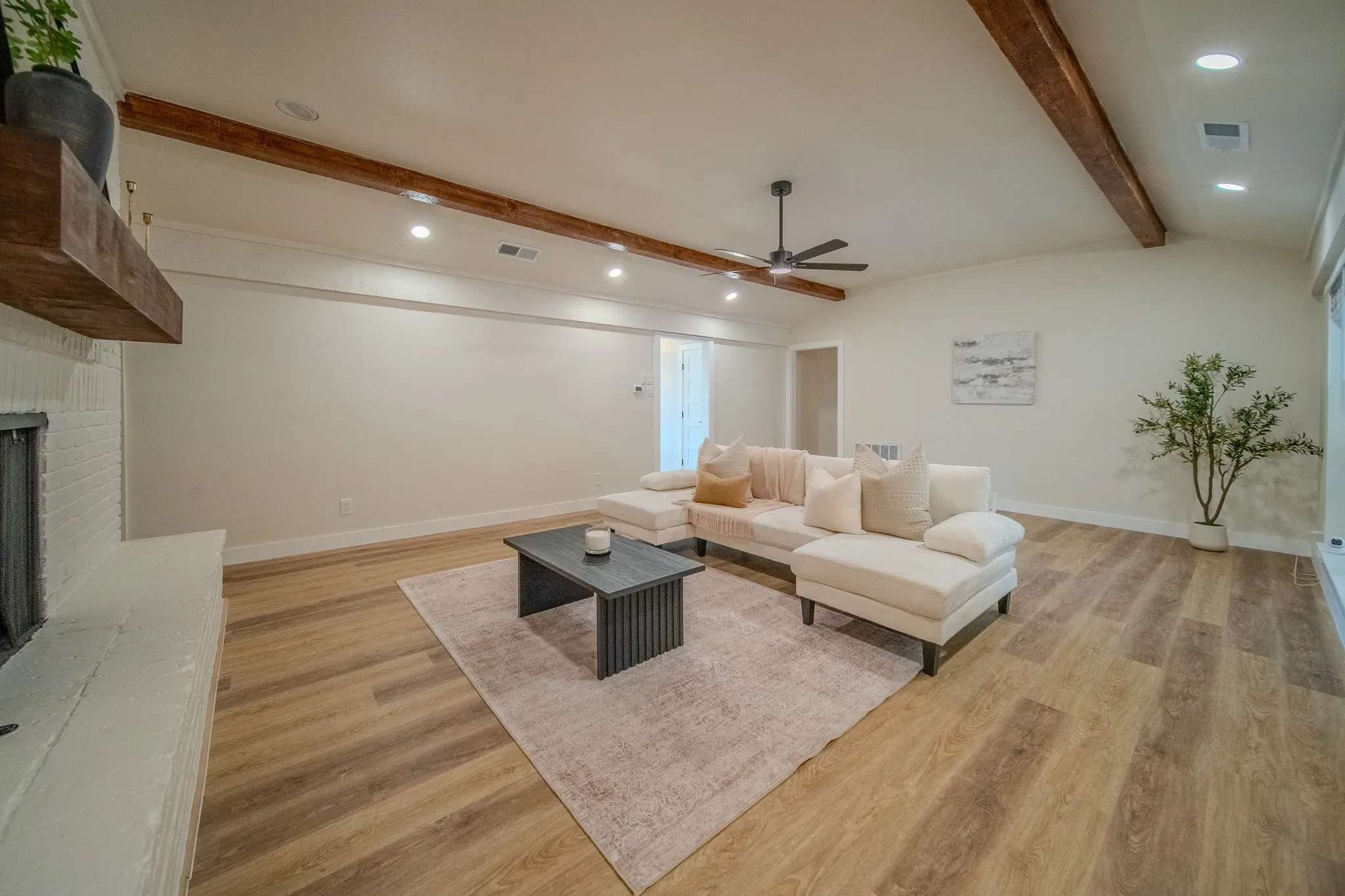 Vaulted ceiling with exposed wood beams, wood-finish flooring, recessed lighting, and a white brick fireplace with a wood mantel