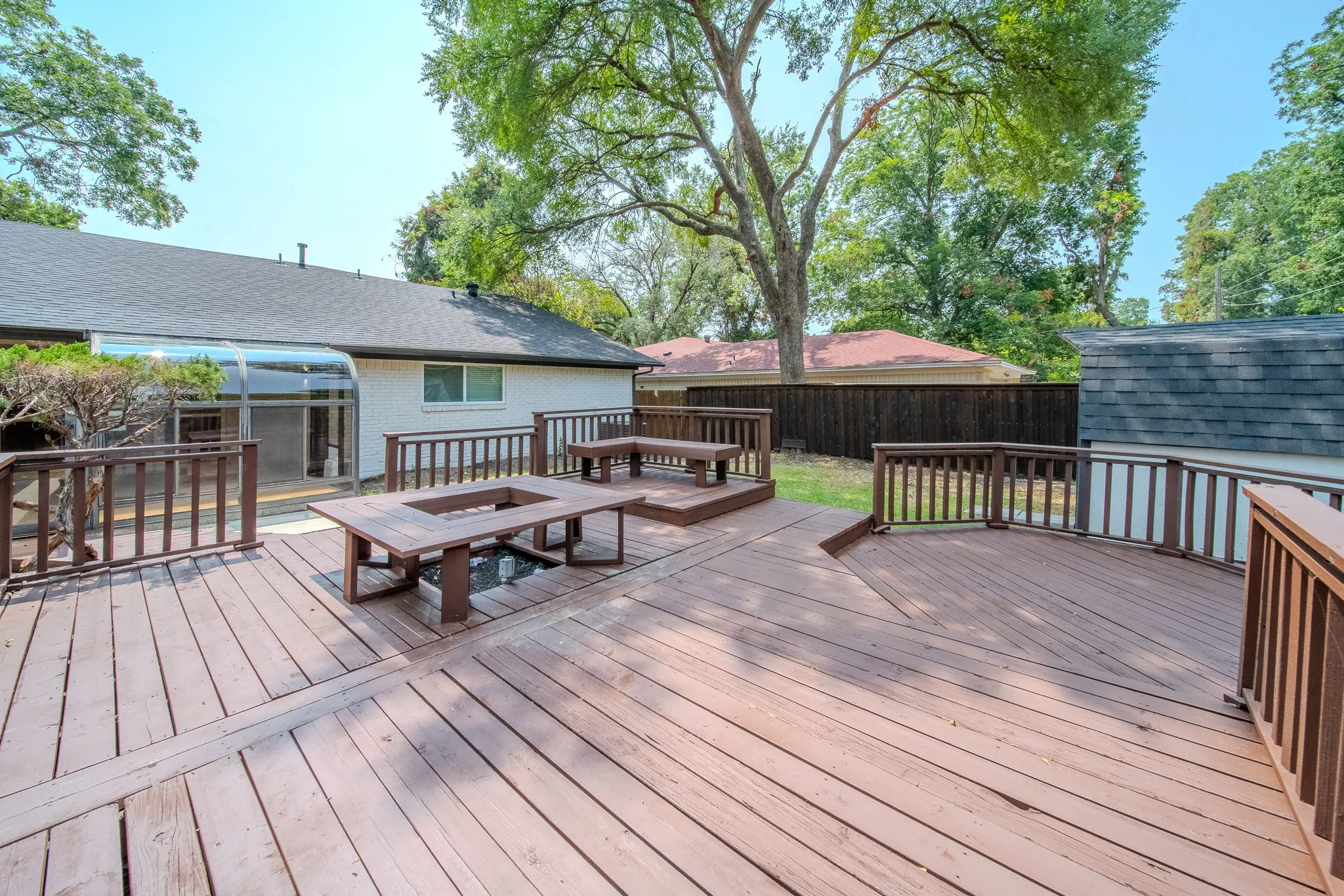 Expansive wooden deck with integrated seating, built-in fire pit, and full railing