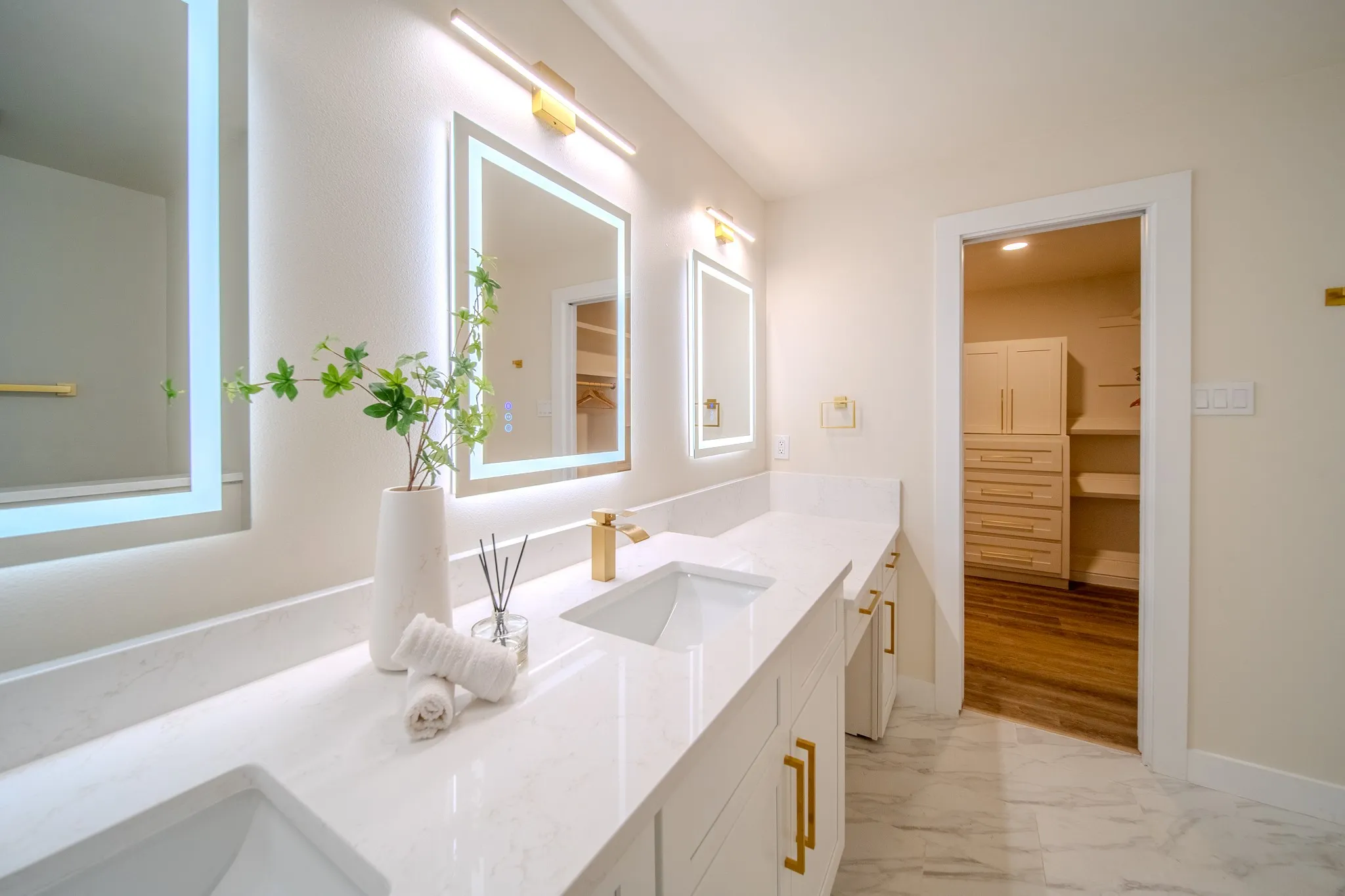 Dual vanity with under-mount sinks, gold-finish fixtures, and integrated lighted mirrors
