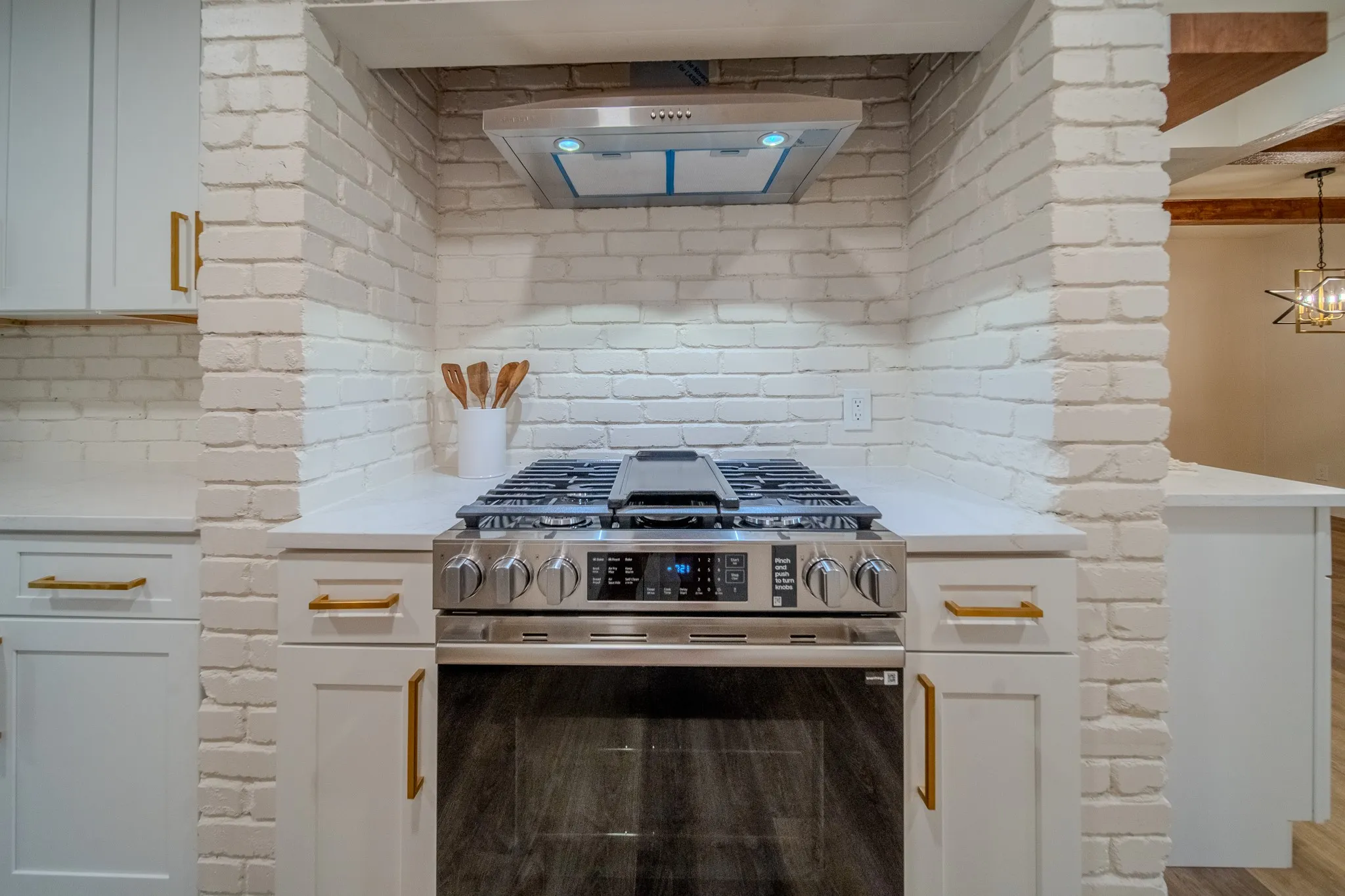 Stainless steel range with a ventilation hood set within a white brick alcove