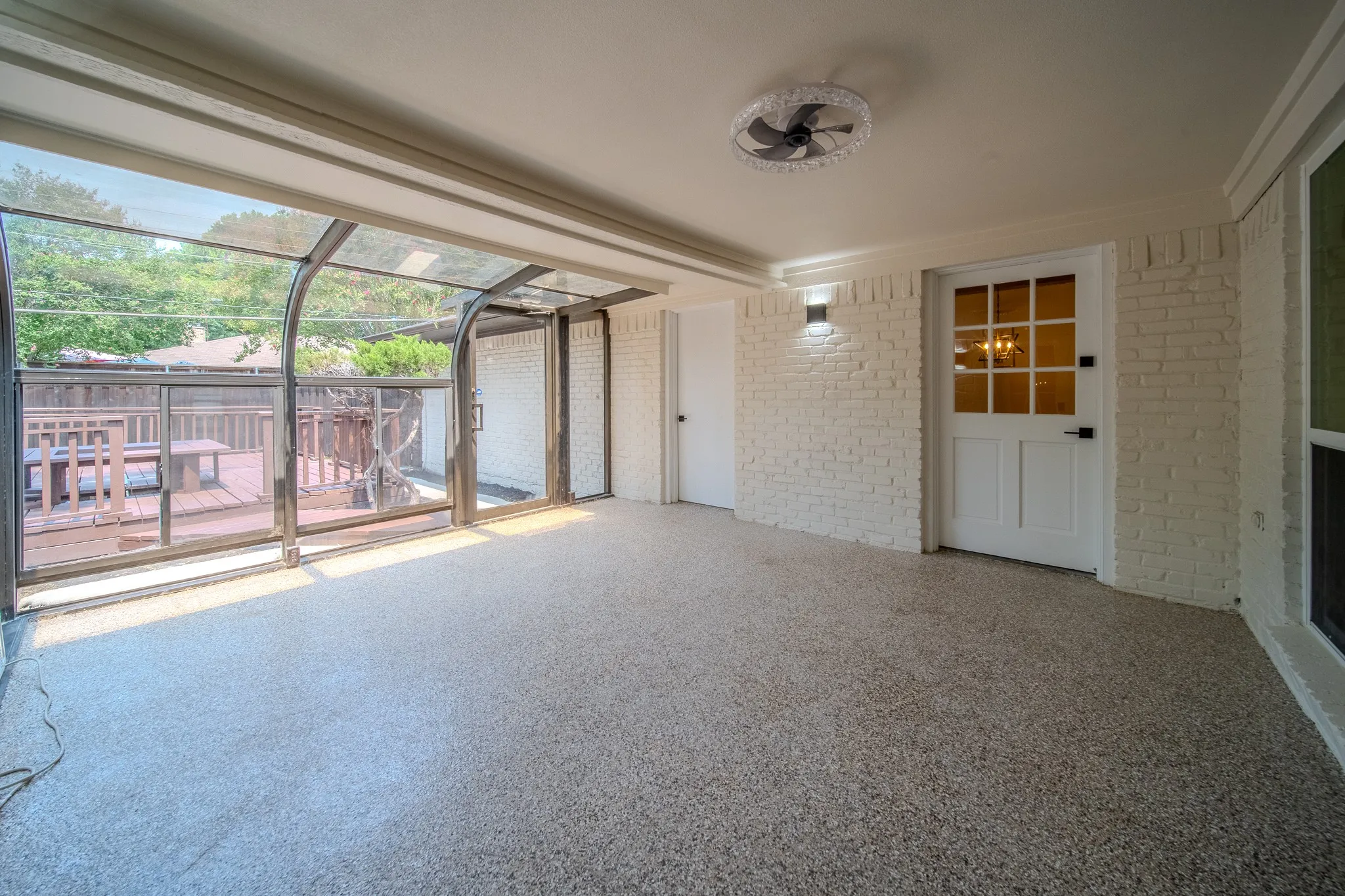 Enclosed patio featuring a retractable glass enclosure, white painted brick wall, patterned flooring, and a ceiling fan