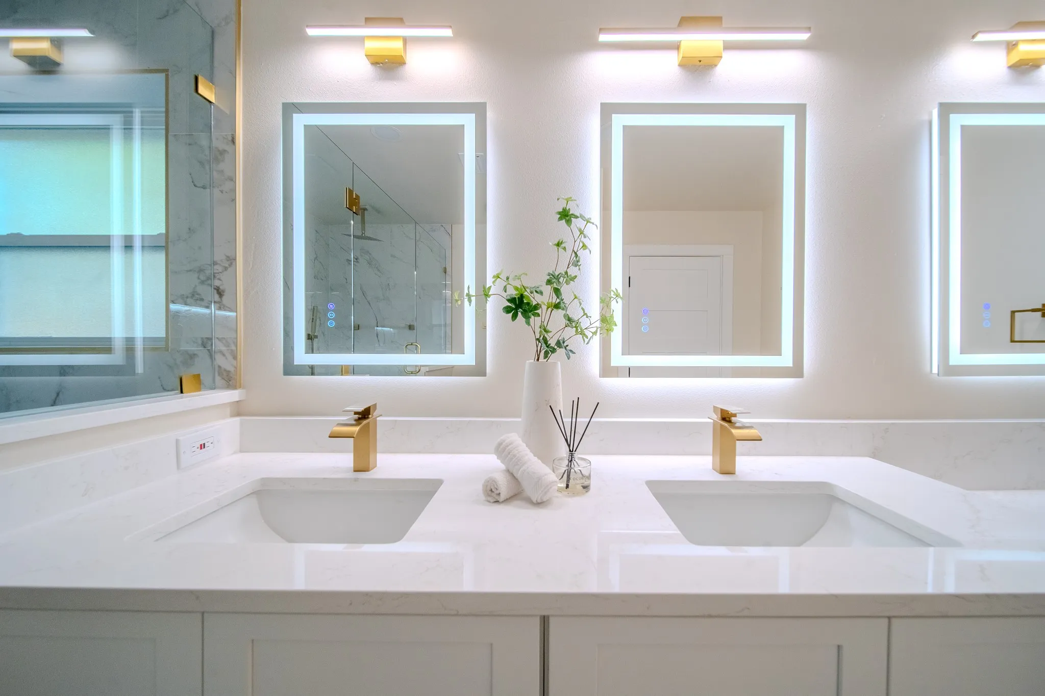 Dual integrated sinks with gold-finish faucets, illuminated mirrors, and white countertops