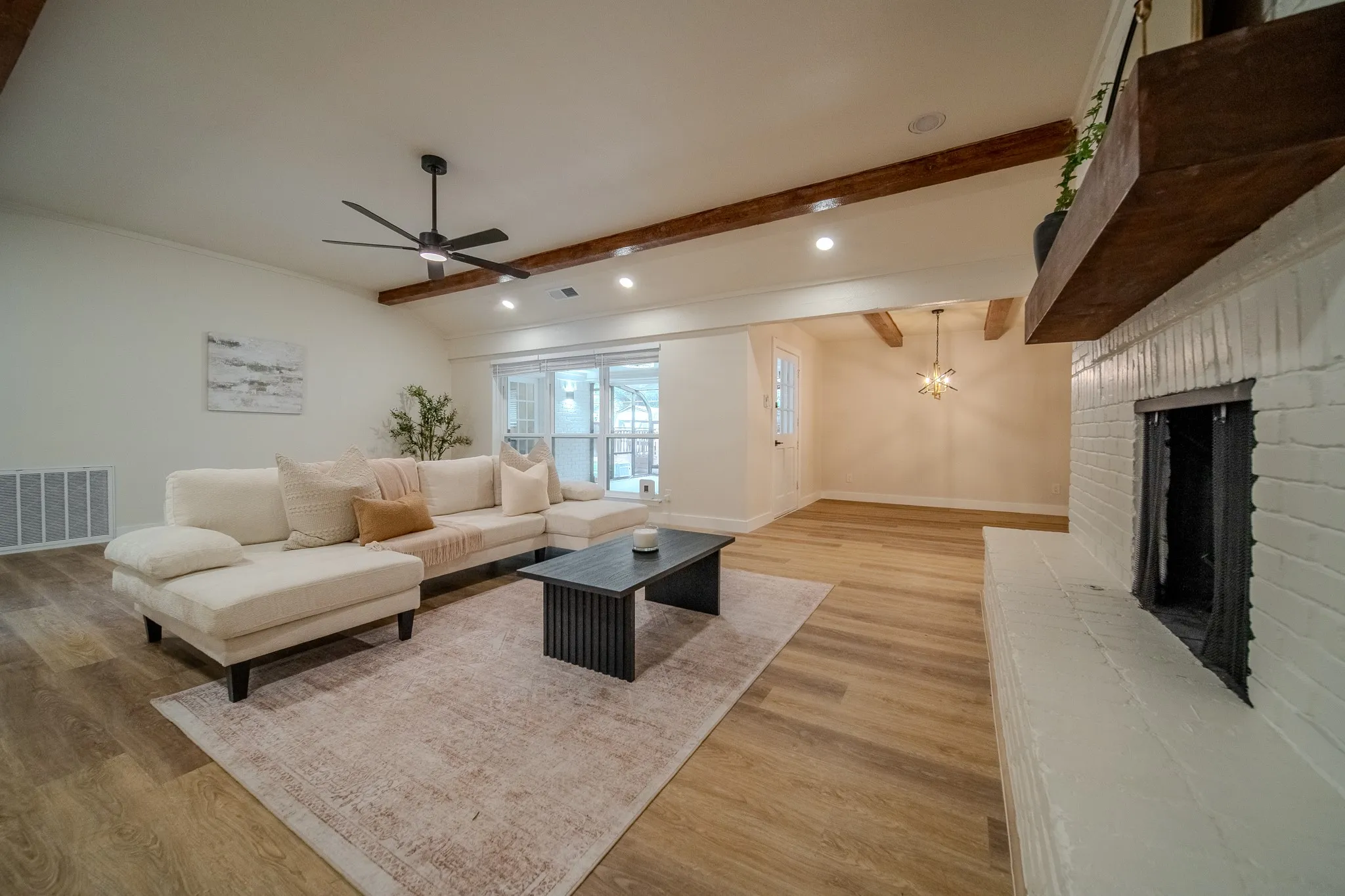 Recessed lighting, wood-finish flooring, exposed ceiling beams, painted brick fireplace, and sliding glass doors