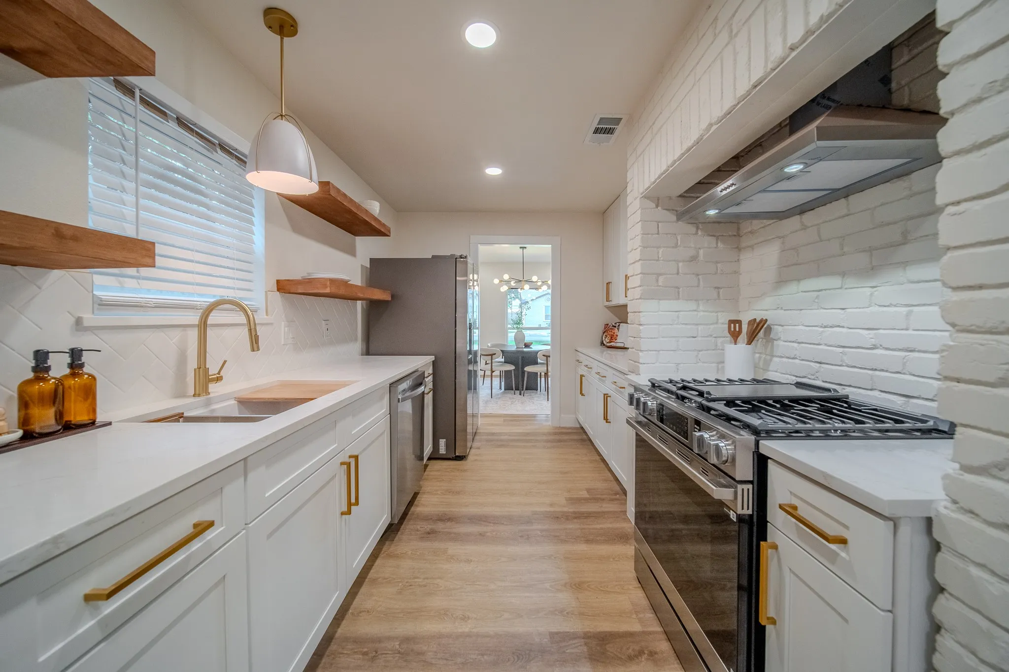 Kitchen featuring white shaker cabinetry, gold-tone hardware, wood-finish flooring, stainless steel appliances, and a white brick-style backsplash