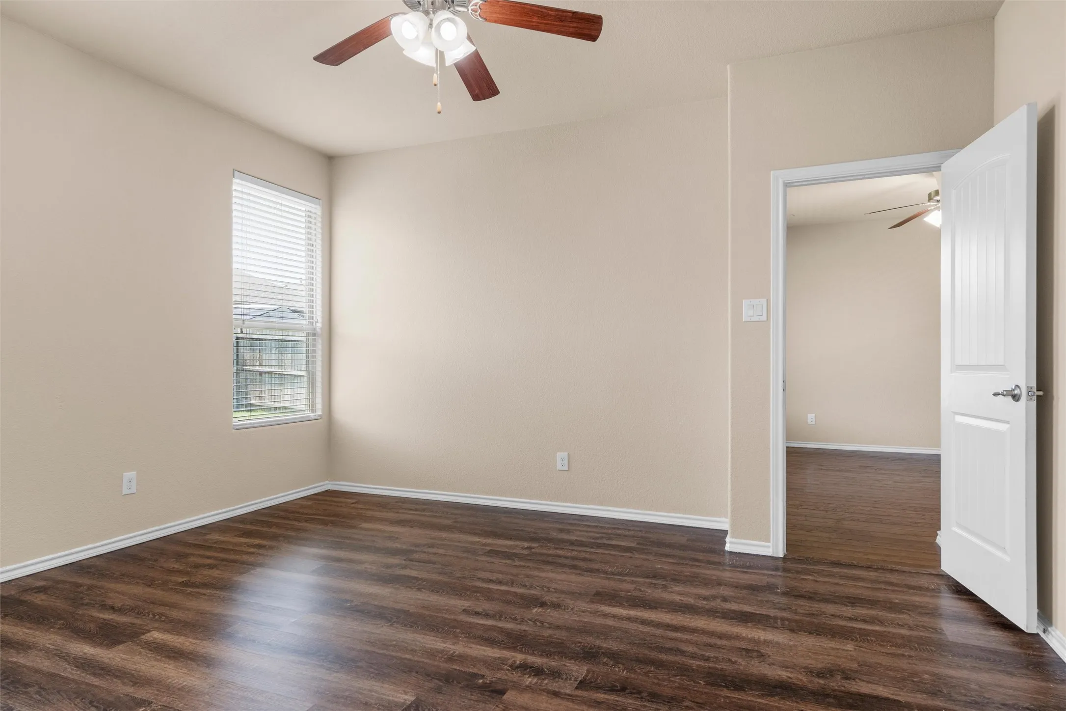 Primary bedroom- Wood-finish flooring throughout, neutral wall tones, and a window with blinds