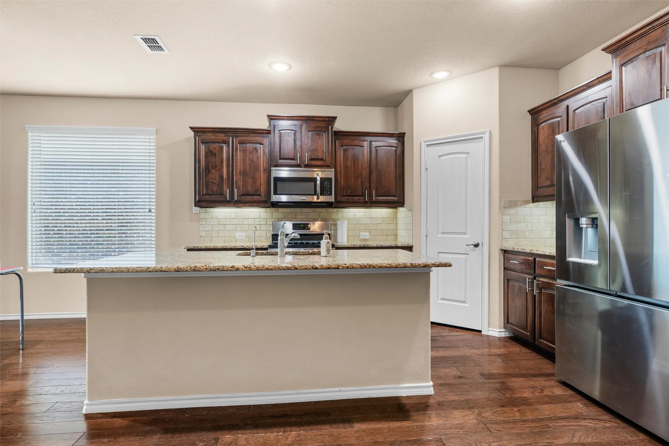 Kitchen with a central island, dark wood cabinetry, stainless steel appliances, tile backsplash, and wood-finish flooring
