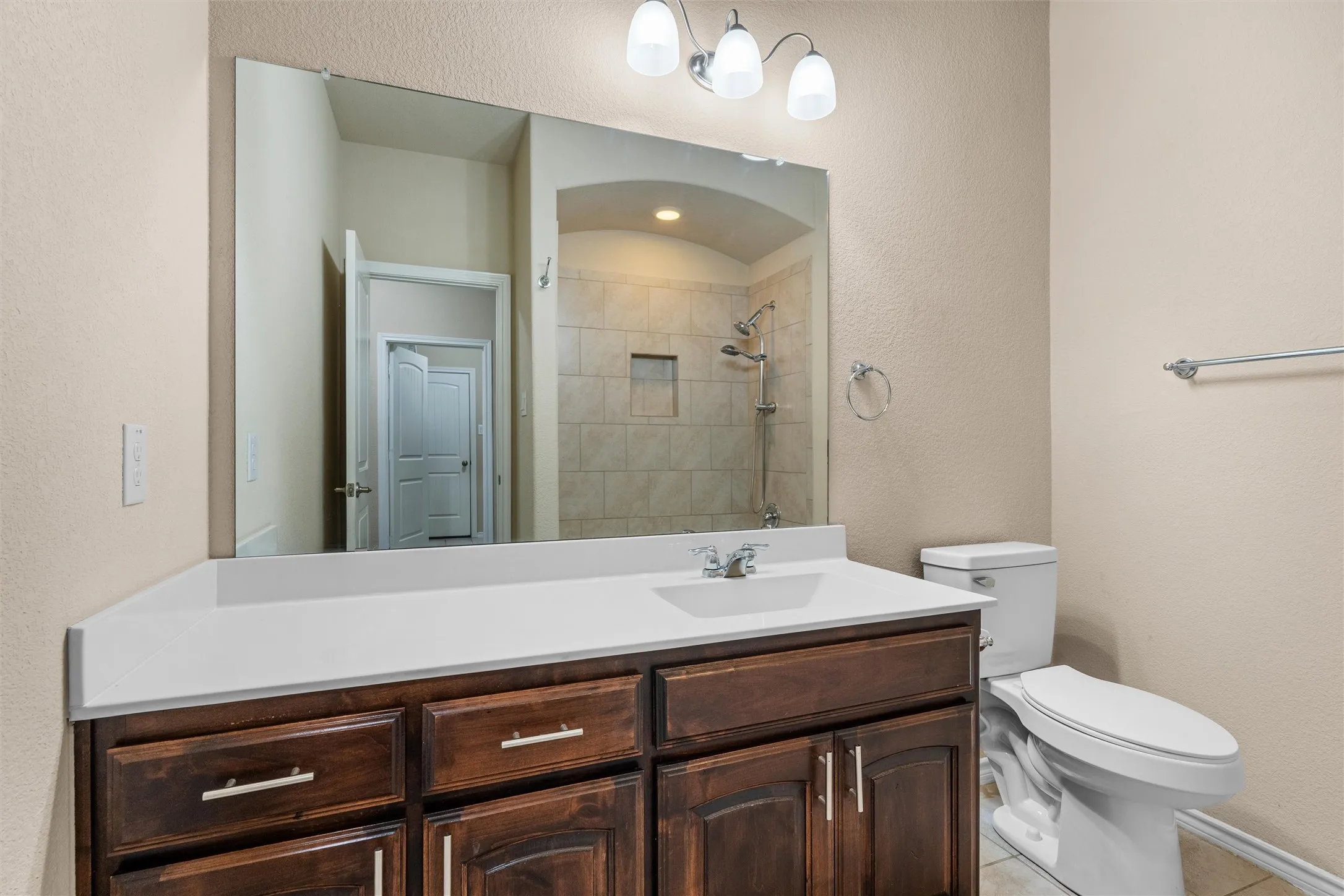 Full bath - Wood-finish vanity cabinetry with a light-toned countertop, a rectangular undermount sink, and a framed mirror