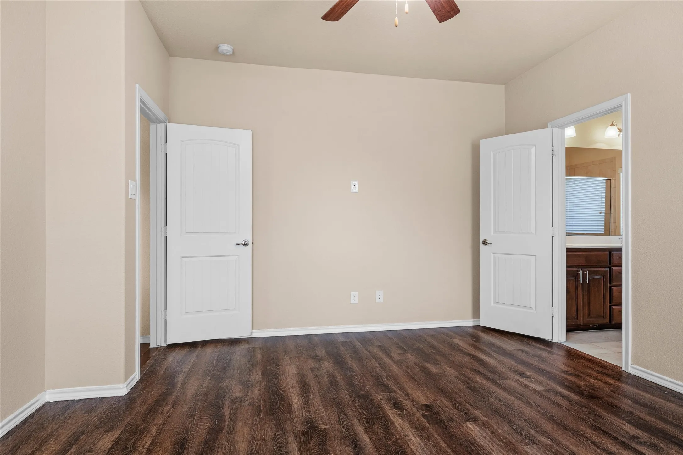 Primary bedroom -  featuring wood-finish flooring, neutral-toned walls, a ceiling fan, and white paneled doors