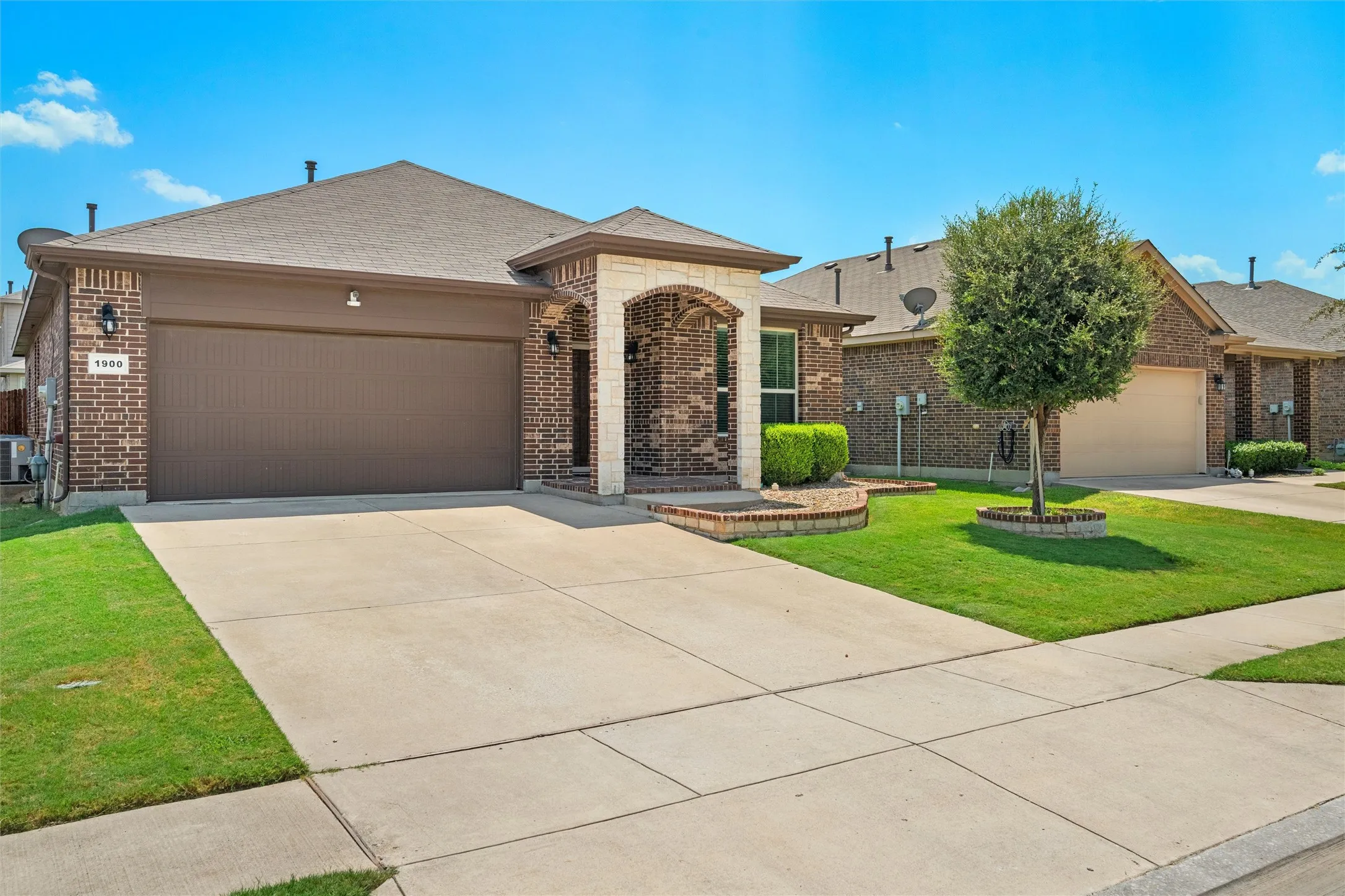 Brick exterior with stone accents, attached two-car garage, concrete driveway, and front lawn landscaping