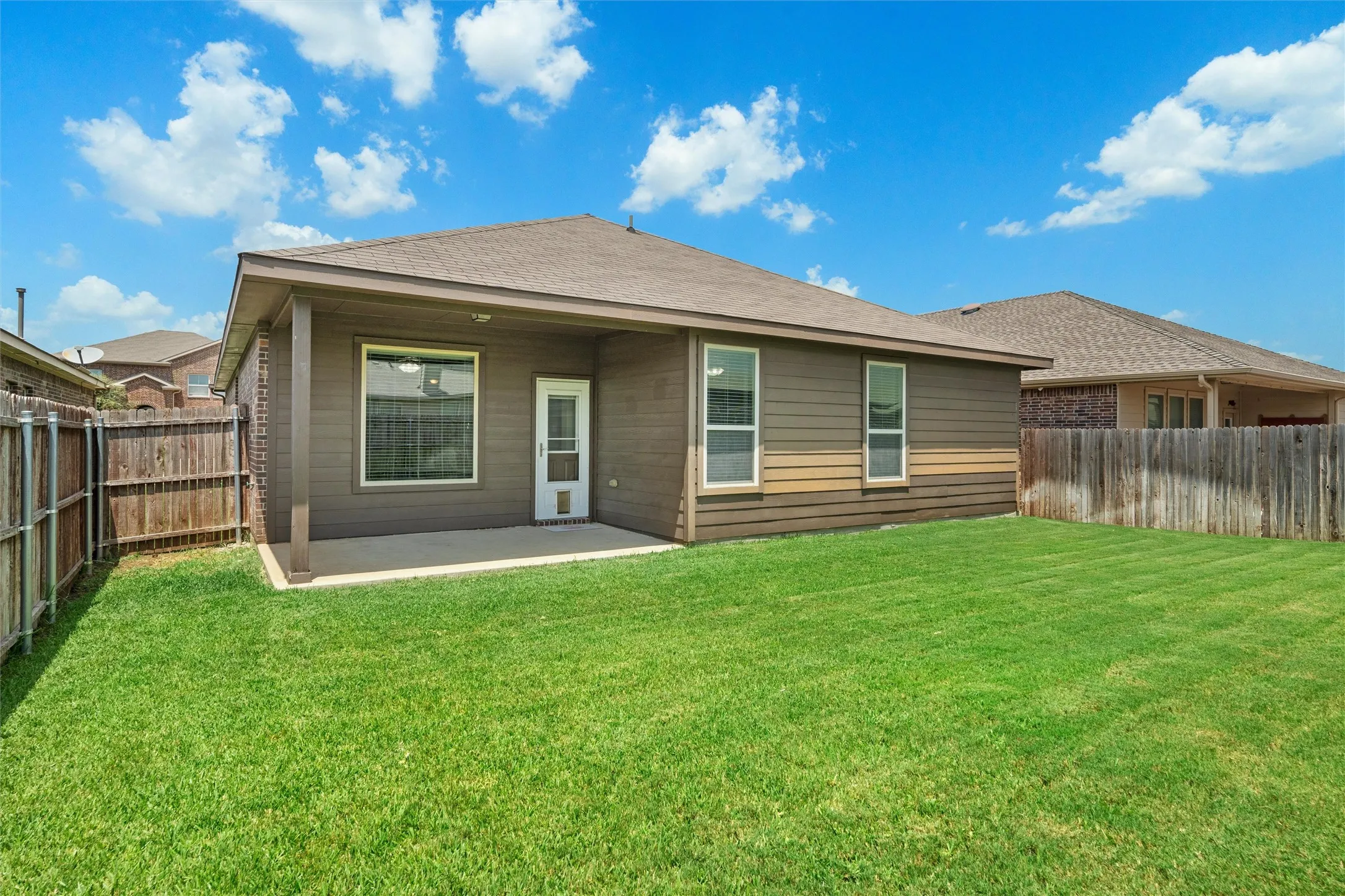 Expansive backyard featuring a manicured lawn, wood fencing, and a concrete patio