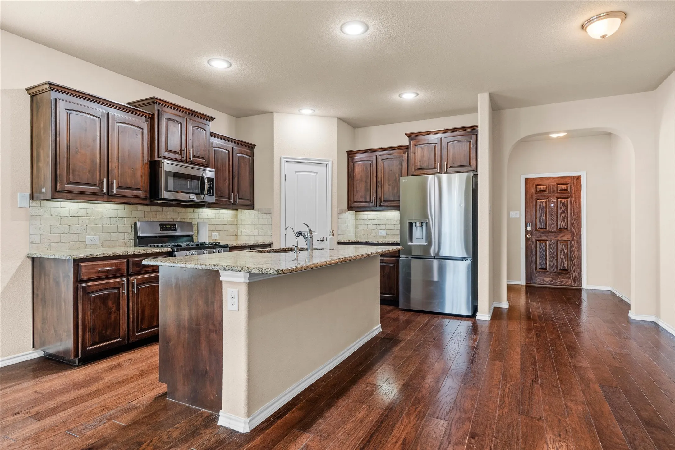 Kitchen featuring wood-finish flooring, dark wood cabinetry, granite countertops, and a subway tile backsplash