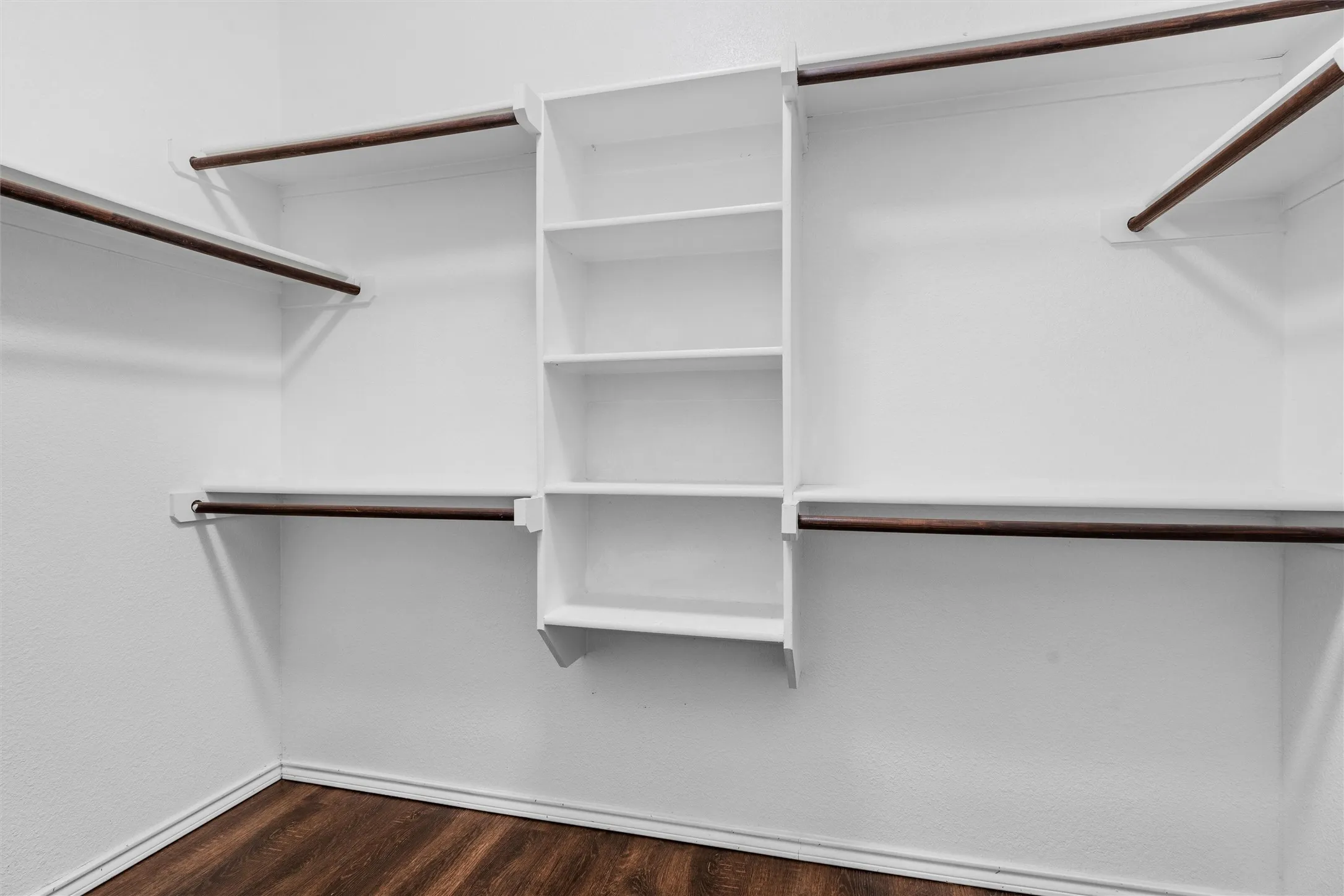 Primary Bedroom Walk in closet - Built-in shelving unit, multiple hanging rods, white wall finish, and wood-finish flooring