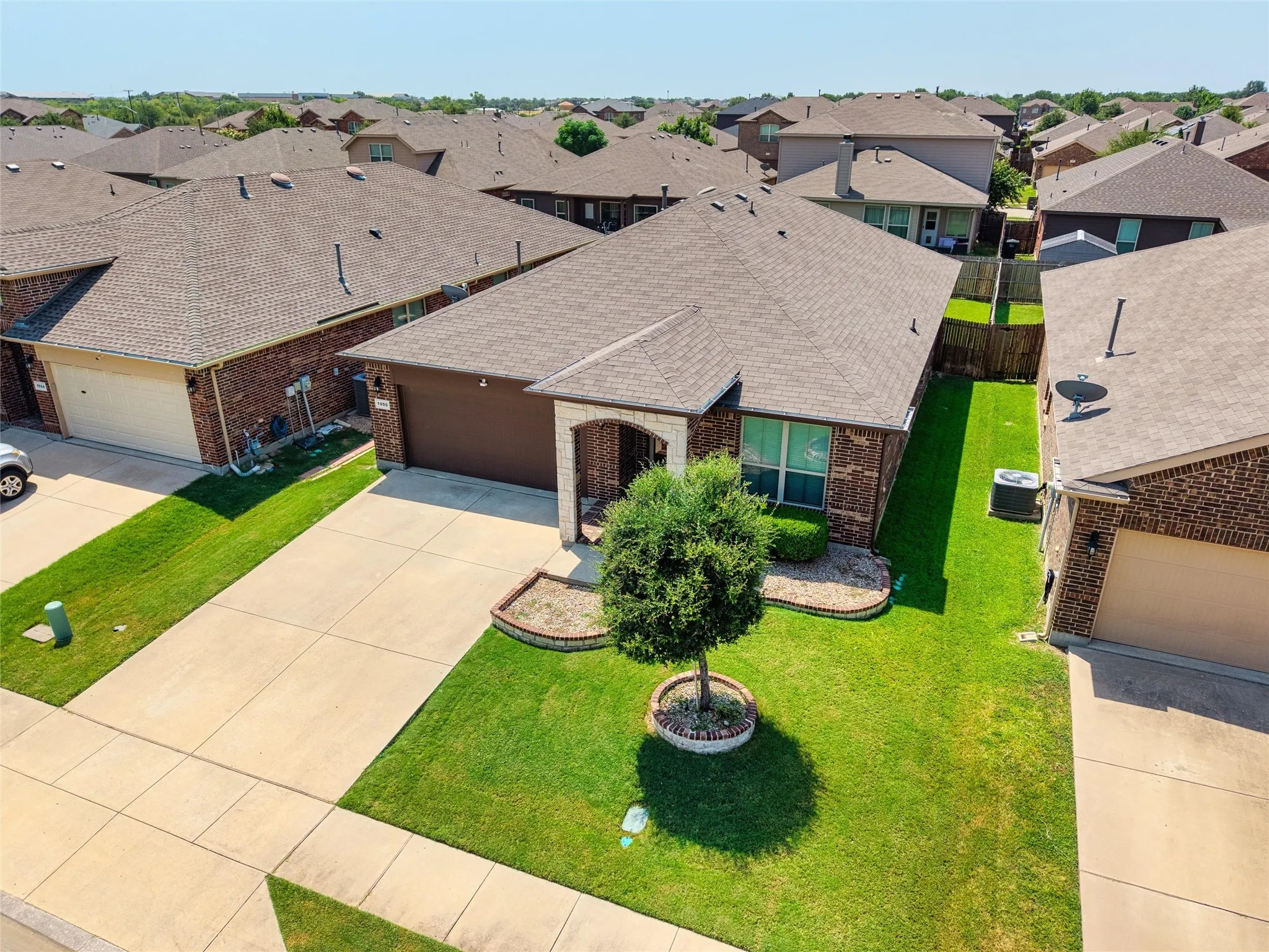 Brick exterior with stone accents, attached garage, concrete driveway, and manicured front lawn