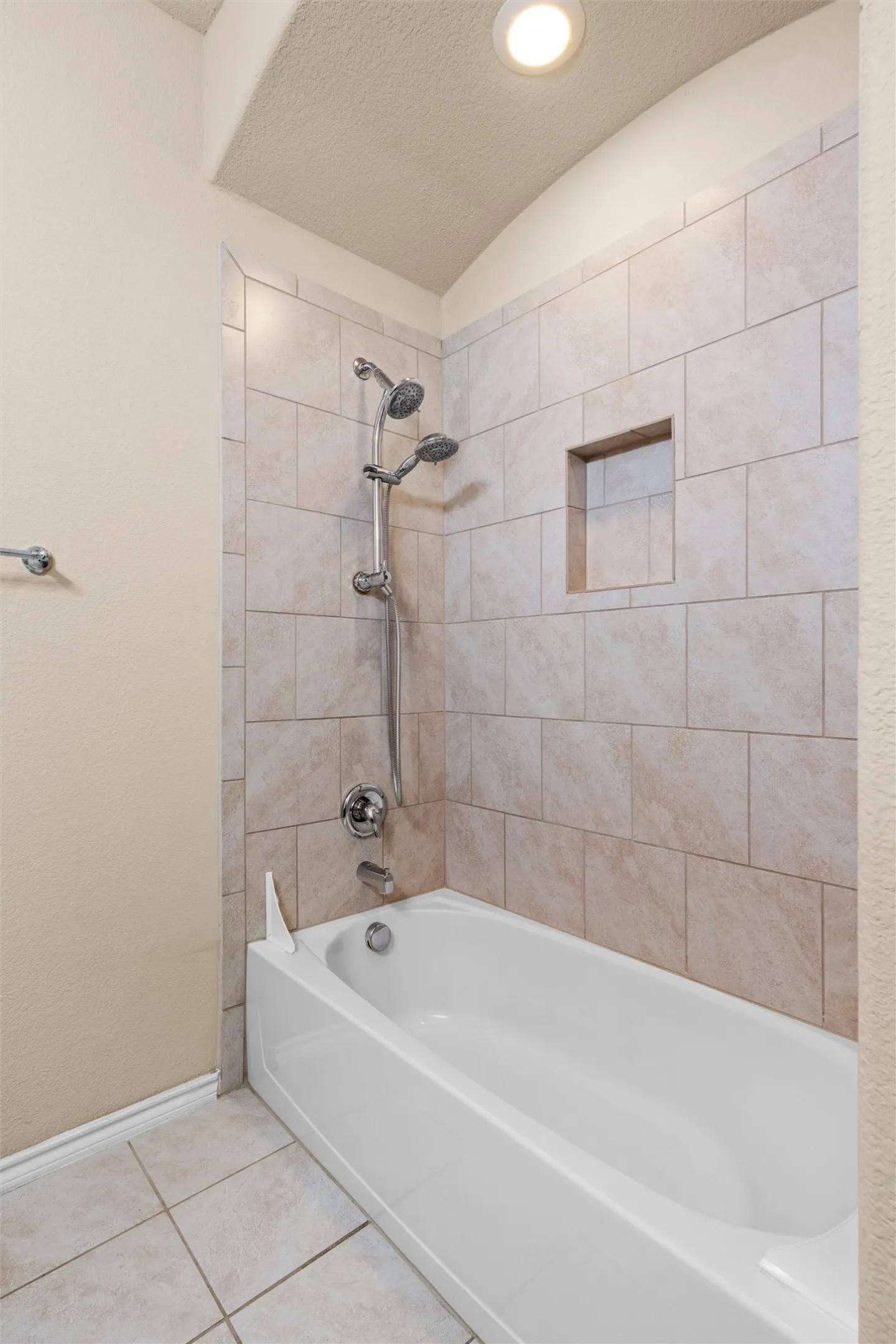 Full bath - Bathtub with light-toned tiled surround, integrated shower niche, and ceiling-mounted recessed lighting