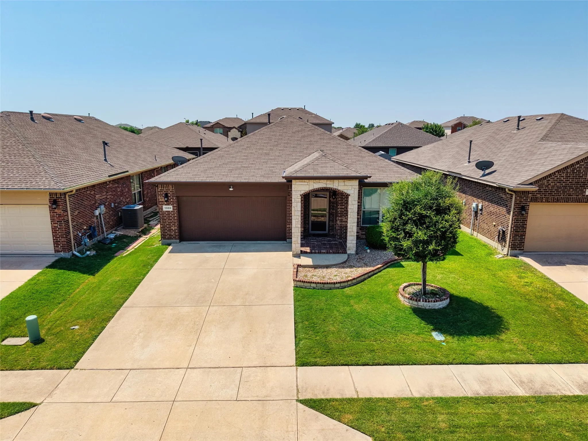 Brick exterior with stone accents, covered entry, attached two-car garage, concrete driveway, and established front landscaping