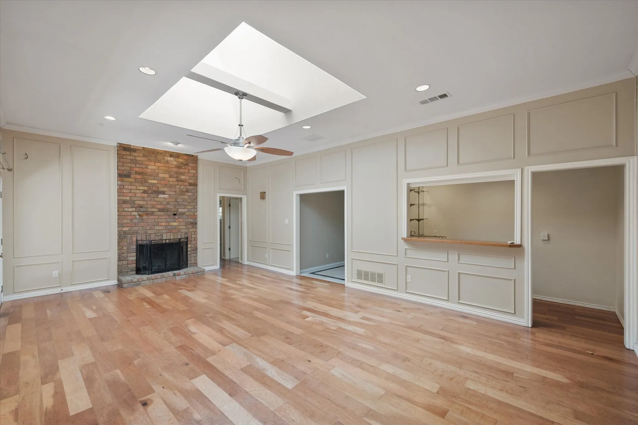 Wood-finish flooring, brick fireplace, skylight, recessed lighting, and built-in serving bar
