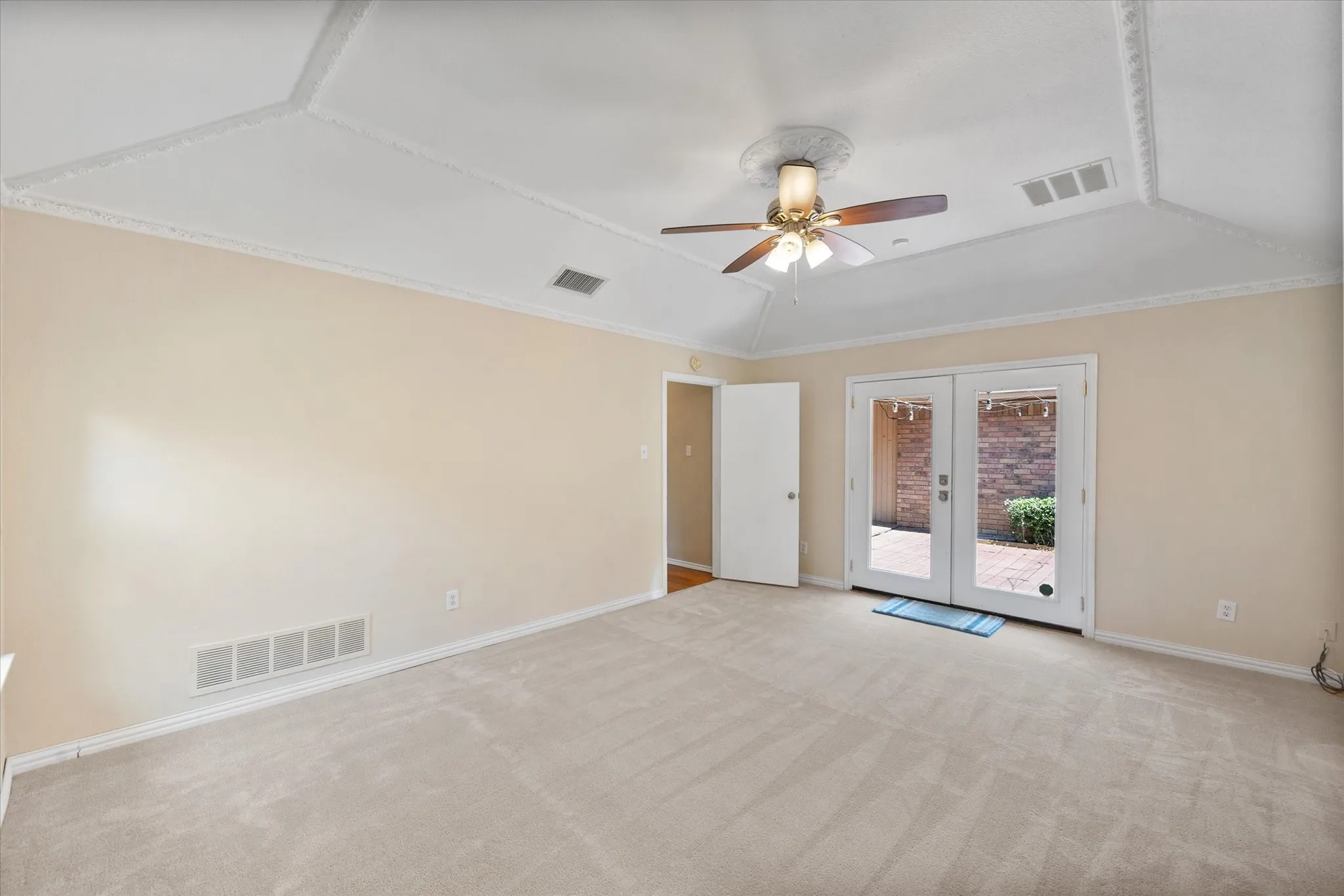 Tray ceiling with decorative molding, ceiling fan, carpet flooring, and French doors to exterior