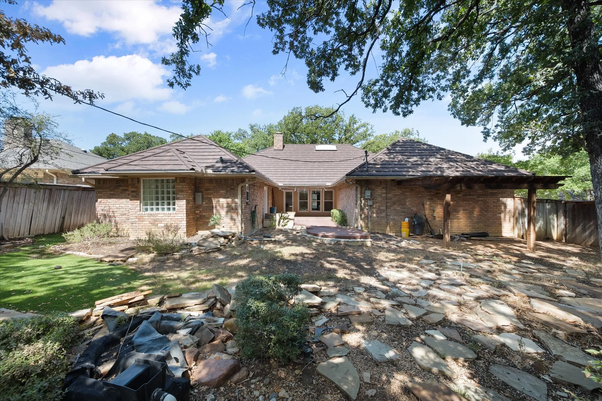Brick exterior with a tiered tile roof, featuring a built-in outdoor structure with a slatted wood roof, and a stone patio