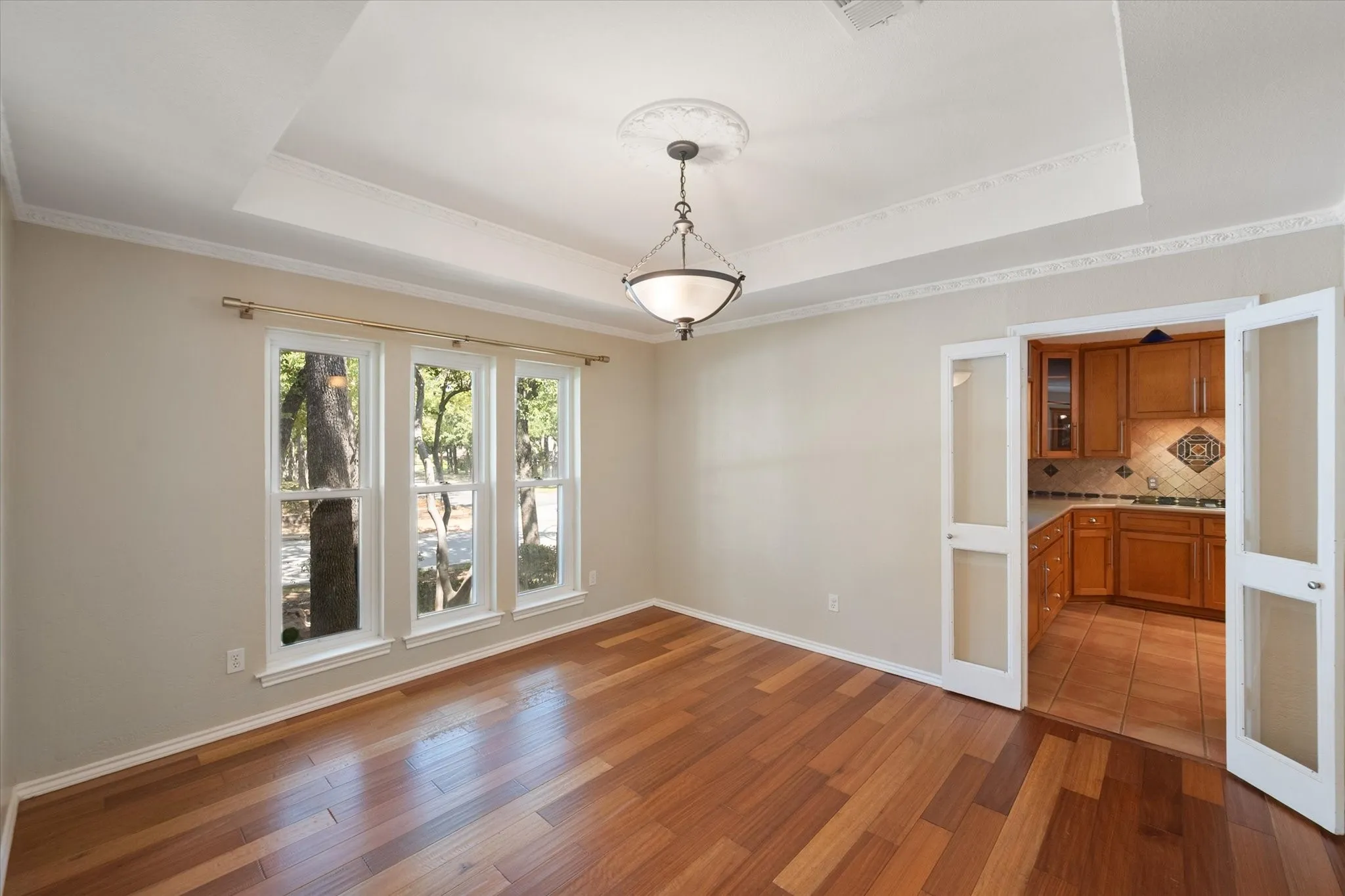 Tray ceiling with detailed crown molding, three large windows, engineered wood flooring and an ornamental chandelier