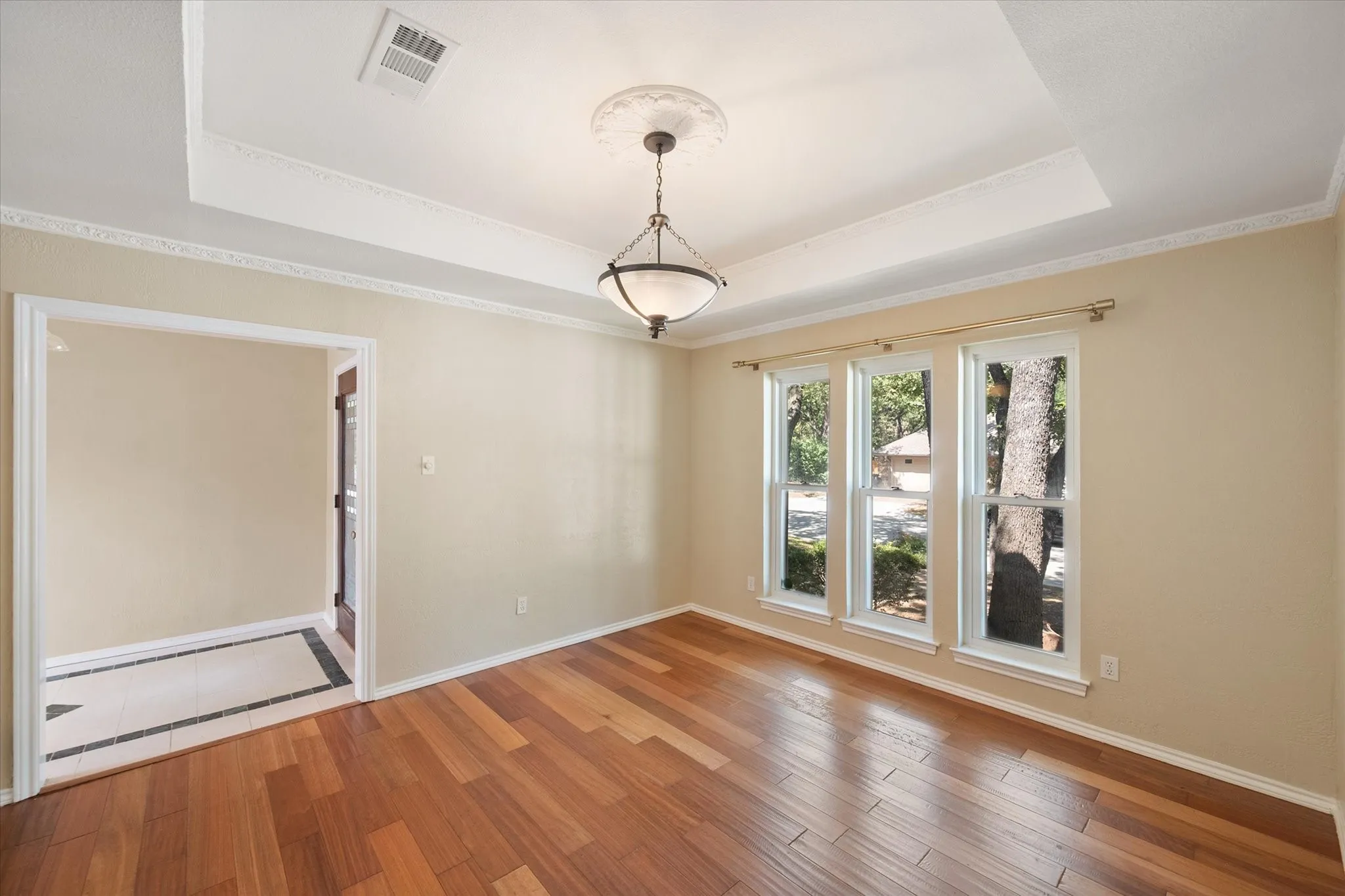 Tray ceiling with detailed crown molding, three large windows, engineered wood flooring and an ornamental chandelier