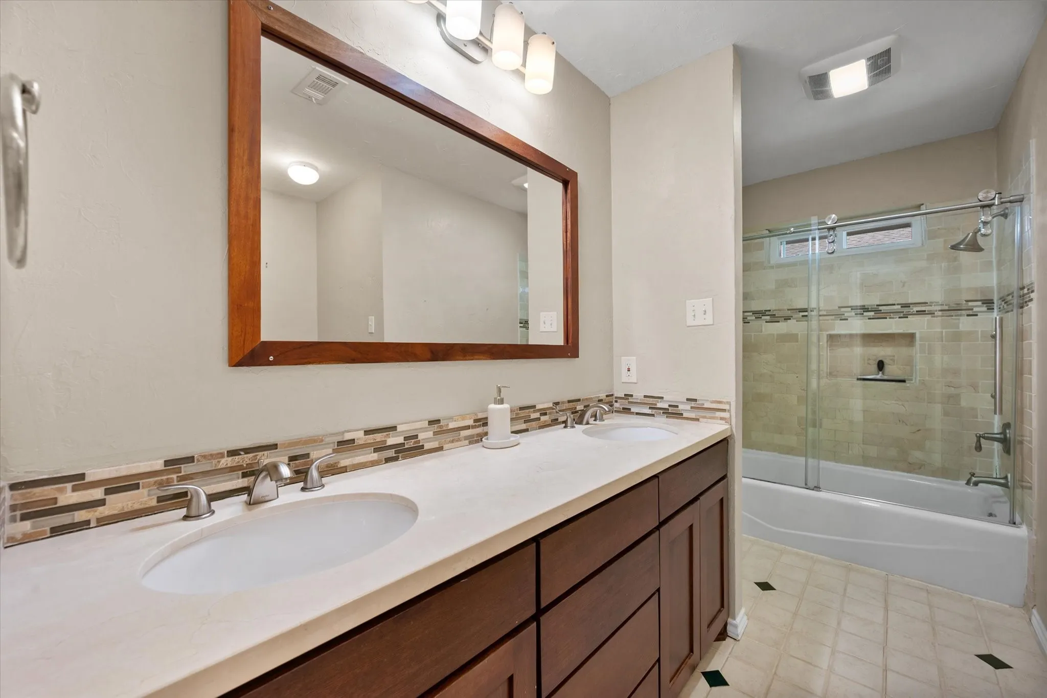 Hall Bathroom Double vanity with undermount sinks, wood-finish cabinetry, and a tile backsplash