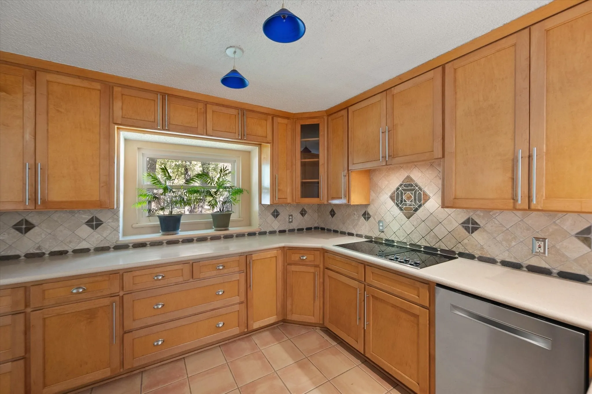 Wood-finish cabinetry, tile flooring, built-in cooktop, stainless steel dishwasher, and a tiled backsplash