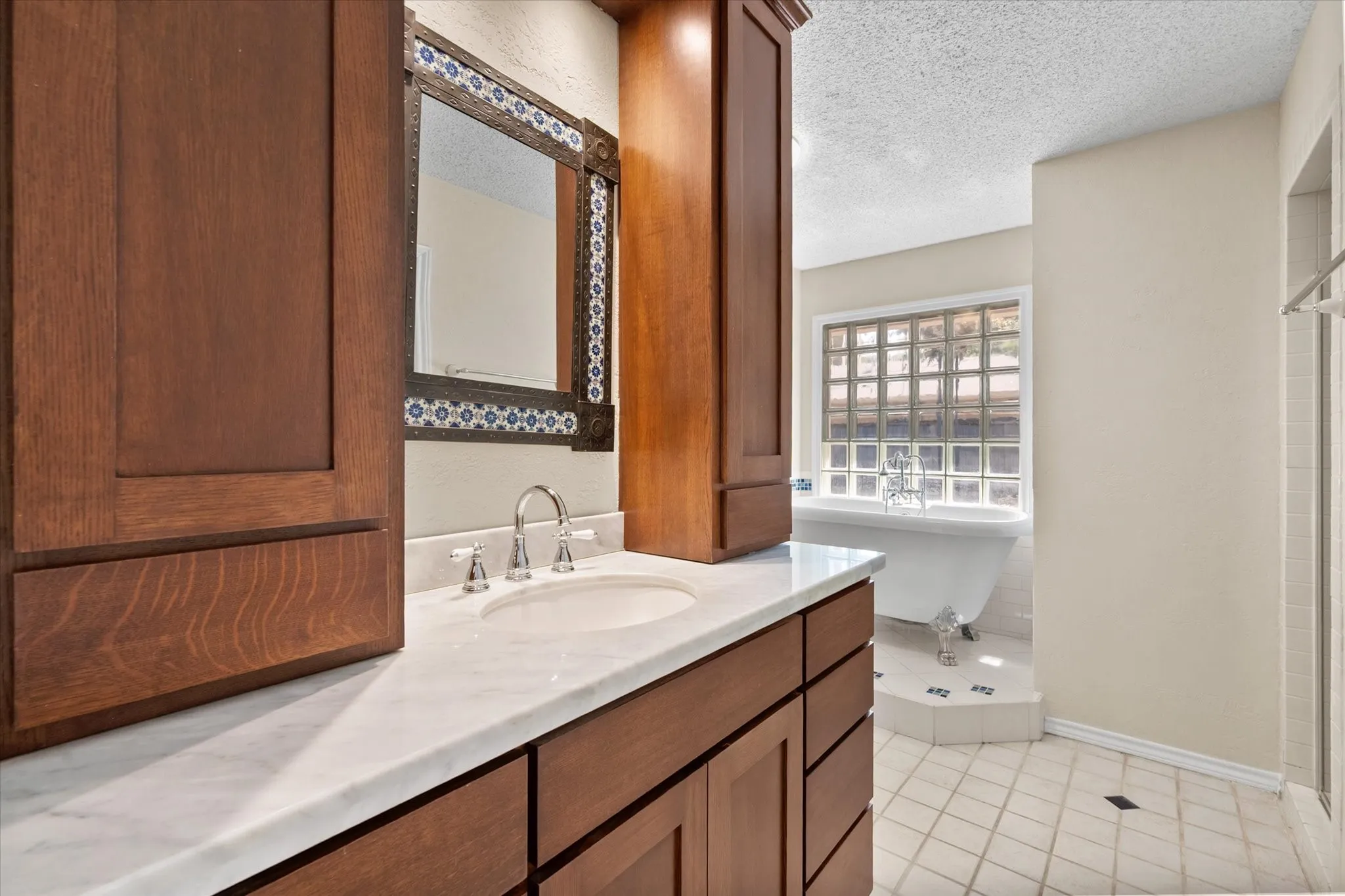 Custom wood cabinetry, white stone vanity top, under-mount sink with chrome faucet, decorative tiled mirror, and clawfoot tub