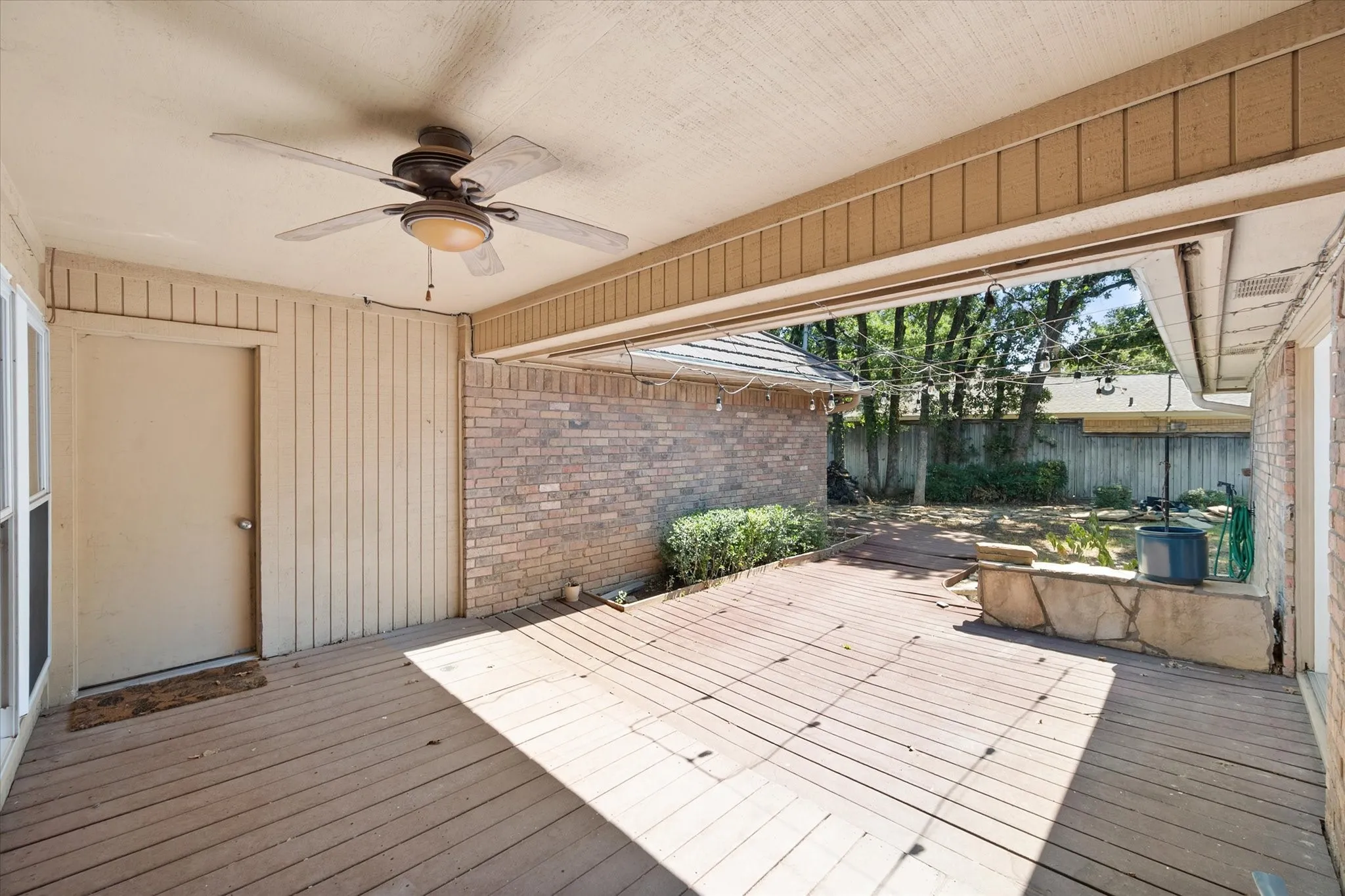 Covered patio with a ceiling fan, wood-finish decking, and brick wall accents