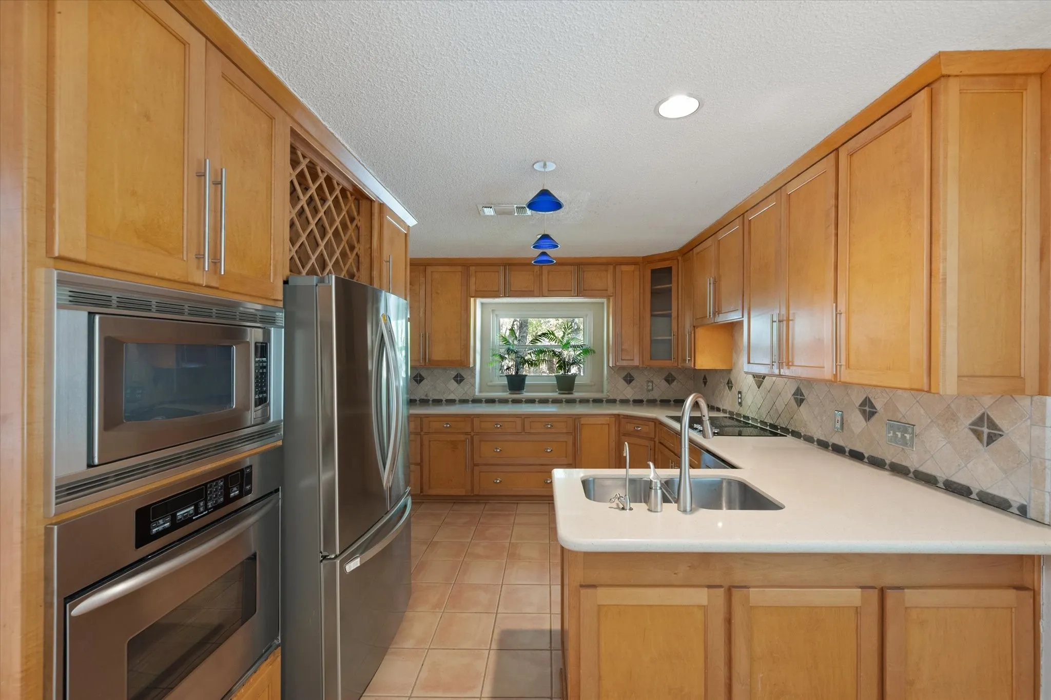 U-shaped kitchen featuring wood cabinetry, stainless steel appliances, a double basin sink, light-toned countertops, and a tiled backsplash