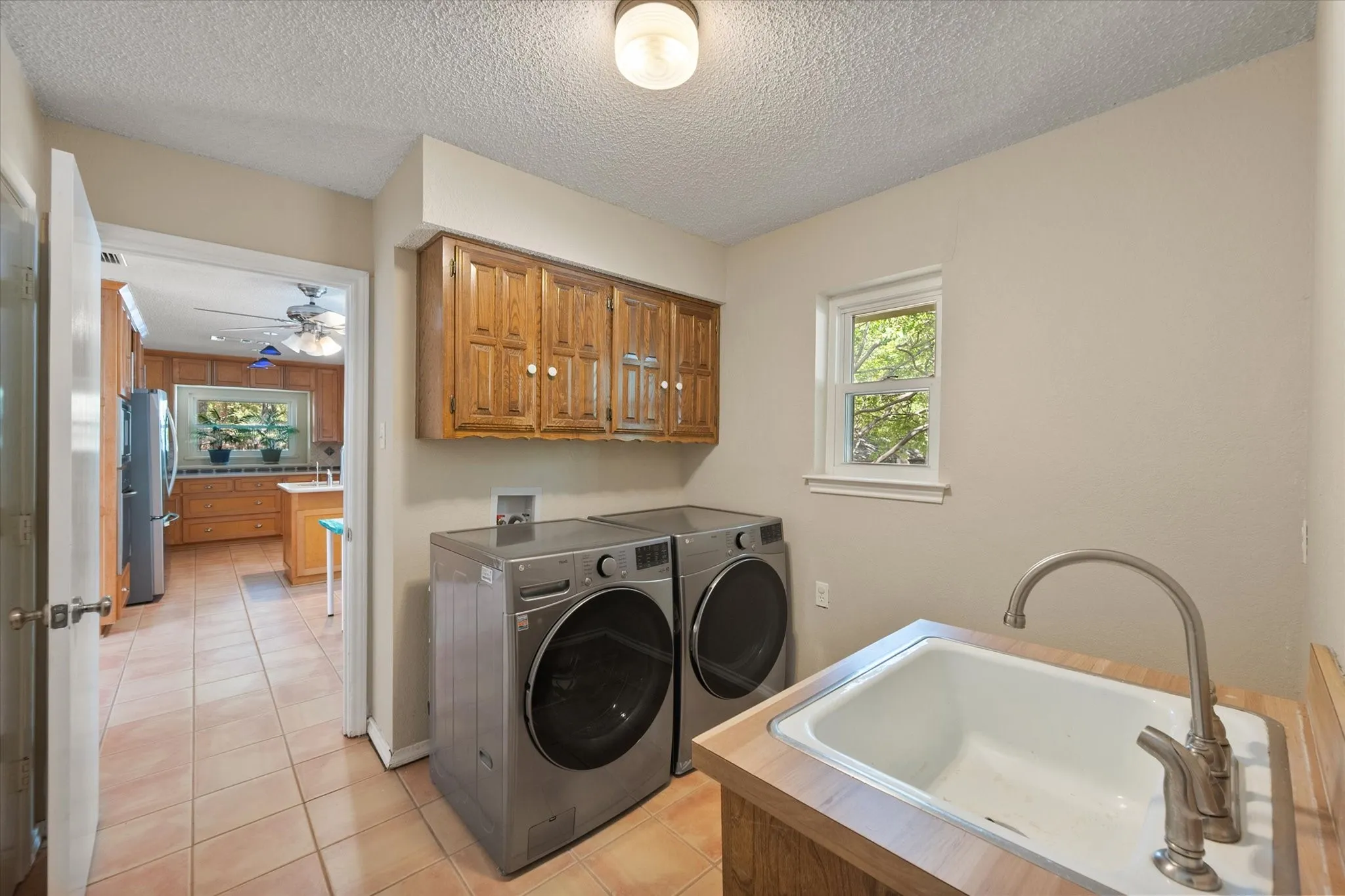 Utility room featuring wood cabinetry, a utility sink with a stainless steel faucet, and a window