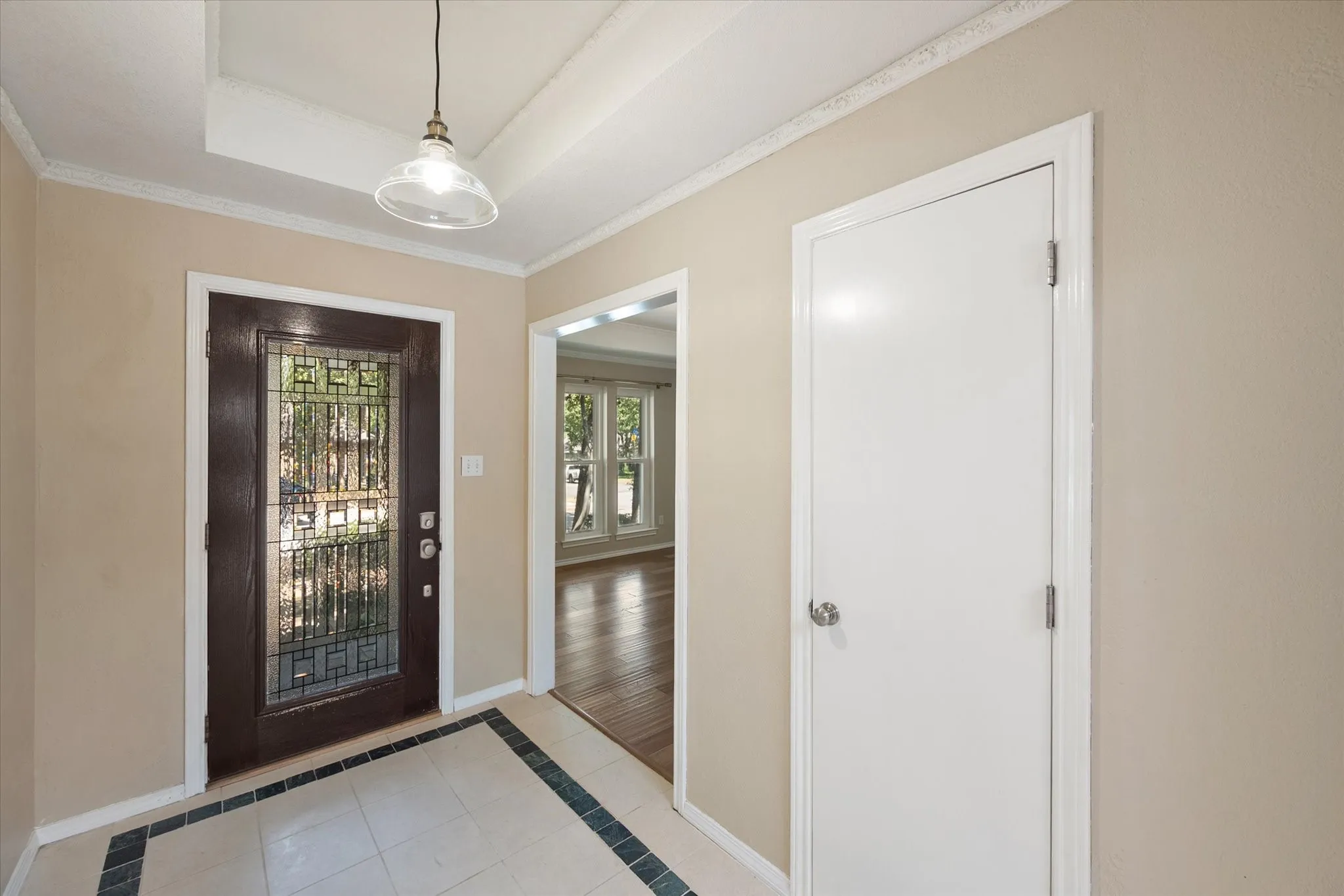 Entryway featuring a dark wood-finish door with decorative glass, cream-colored tile flooring with a dark border, a single pendant light fixture, and crown molding