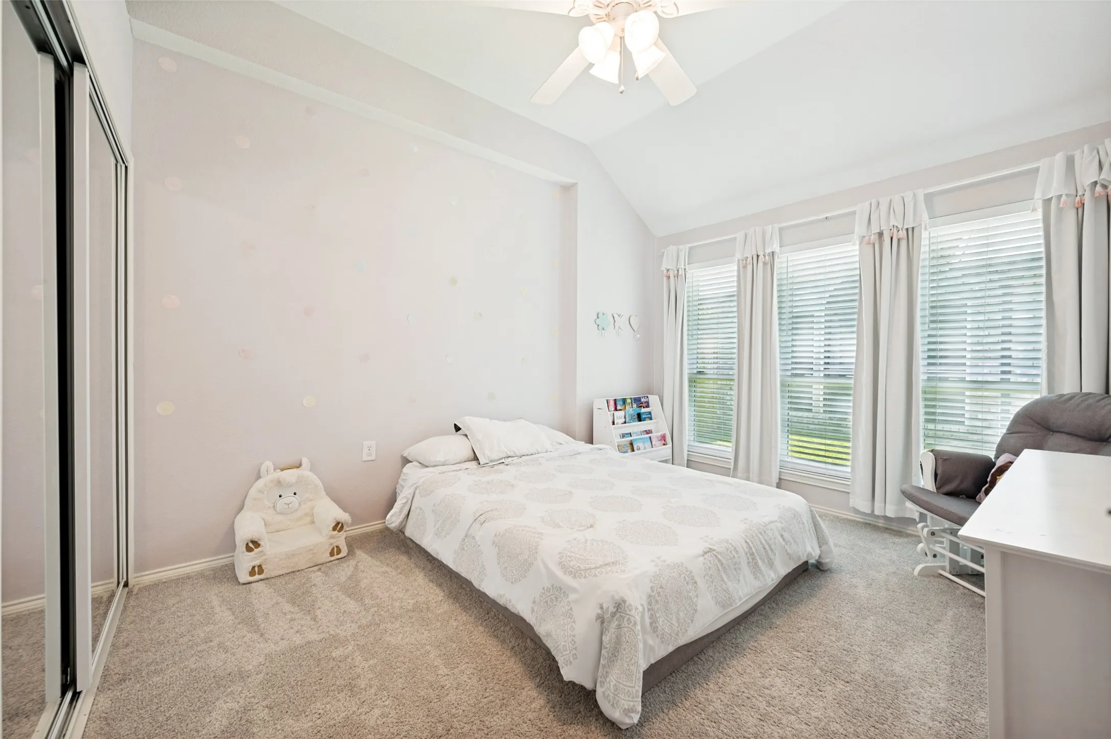 Vaulted ceiling with a ceiling fan, mirrored closet doors, carpeted flooring, and multiple windows with blinds