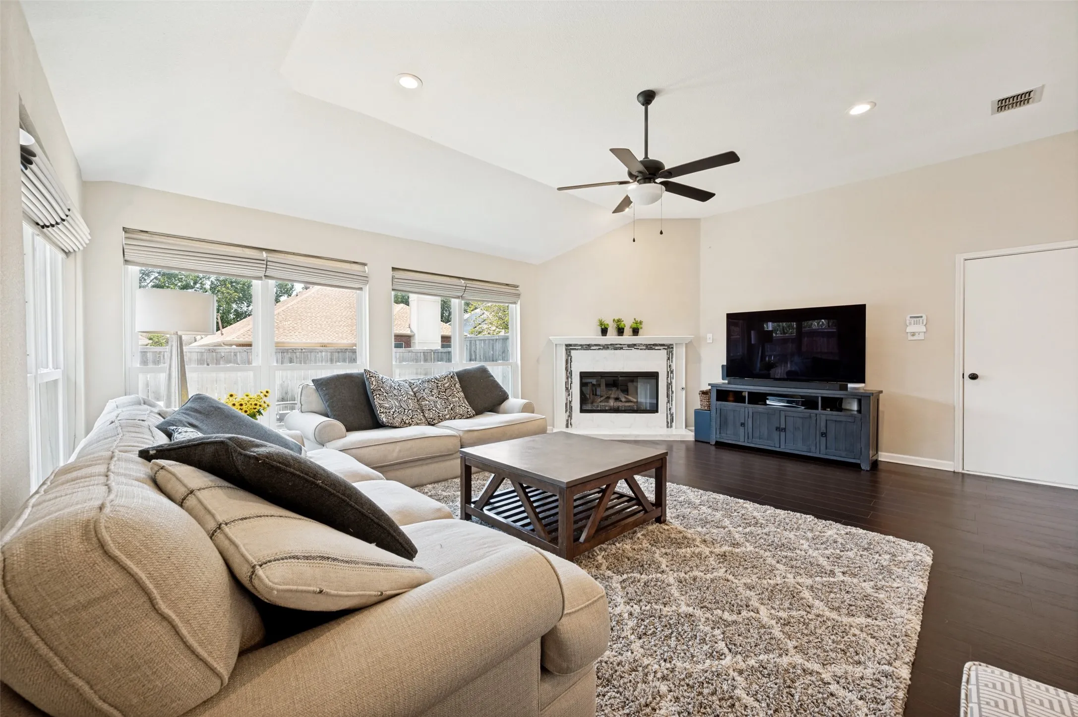 Spacious living area featuring dark wood-finish flooring, a corner fireplace with a tiled surround, recessed lighting, and a ceiling fan