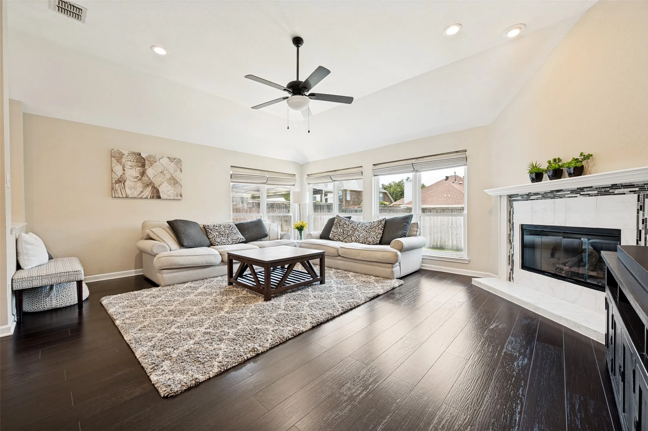 Vaulted ceiling with recessed lighting and ceiling fan, dark wood-finish flooring, multiple windows with blinds, and a fireplace with a tiled surround