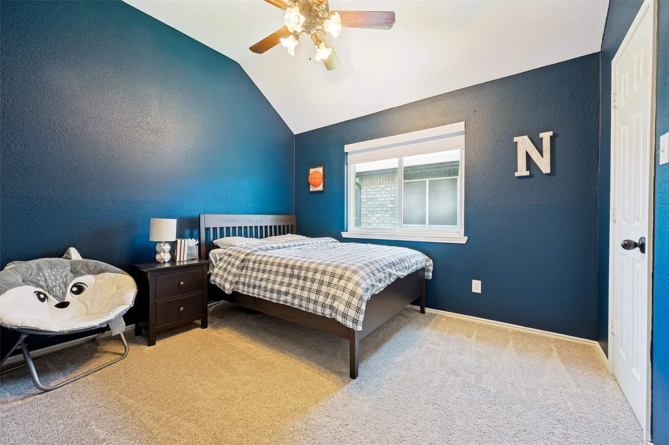 Vaulted ceiling with a ceiling fan, window with privacy blind, plush carpet, and a paneled door with dark hardware