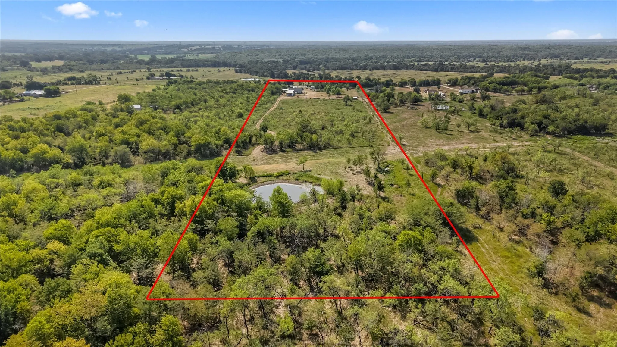 Expansive acreage with diverse tree cover, open clearing, and a natural pond