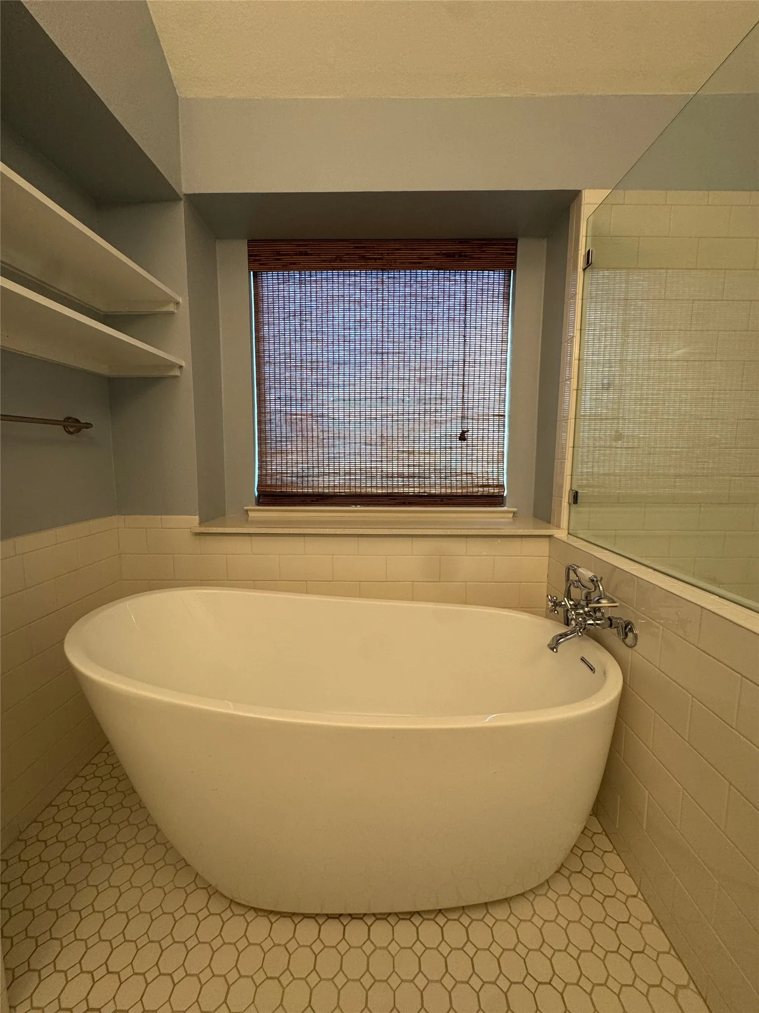 Freestanding soaking tub with chrome fixtures, subway tile wainscoting, and mosaic tile flooring