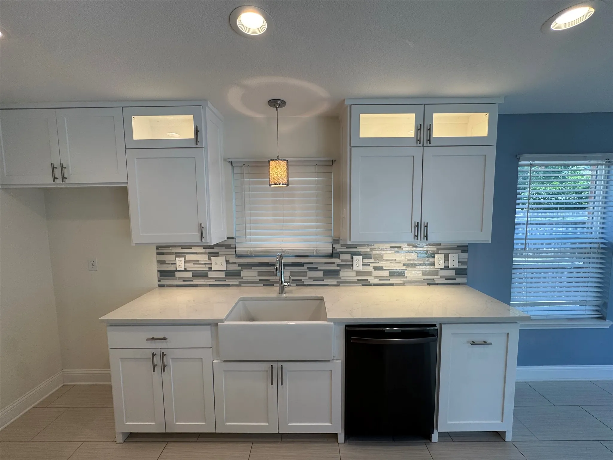 White shaker cabinetry with dark hardware, a farmhouse-style sink, a mosaic tile backsplash, recessed lighting, and a contemporary pendant light fixture