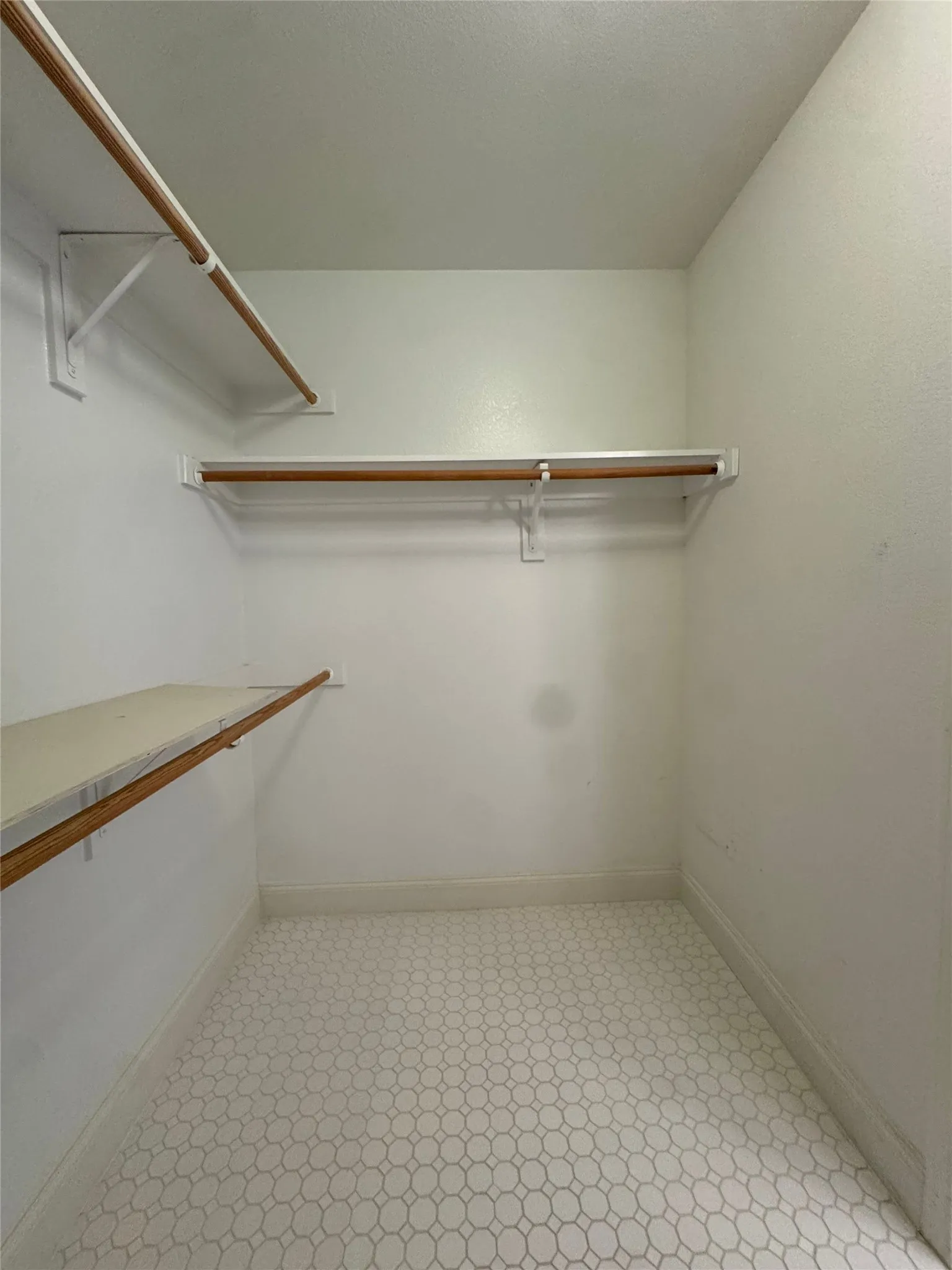 Walk-in closet featuring white walls, multi-level shelving, and a patterned floor