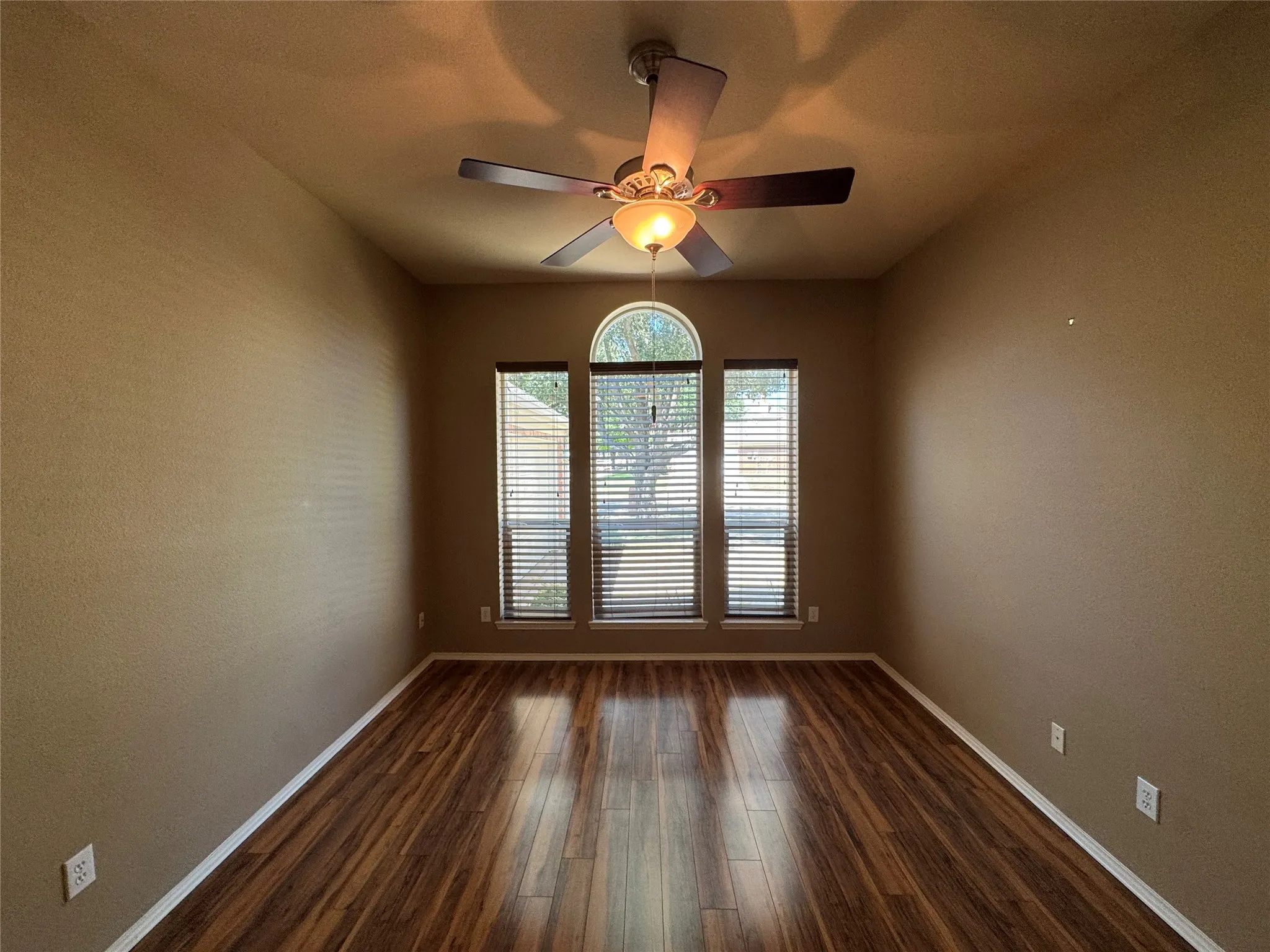 Wood-finish flooring, ceiling fan with integrated lighting, and multiple windows with blinds